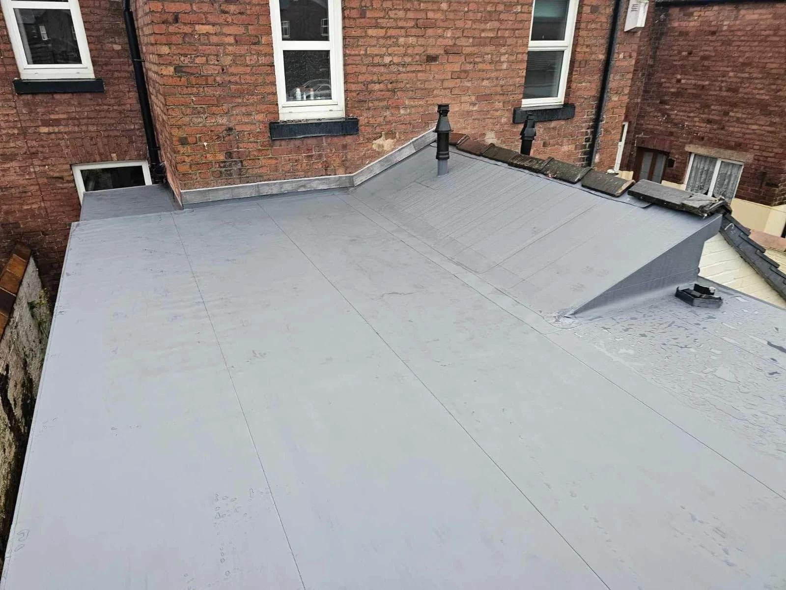 Large residential flat roof project in Carlisle showing clean membrane lines and expert flashing against an older brick building.