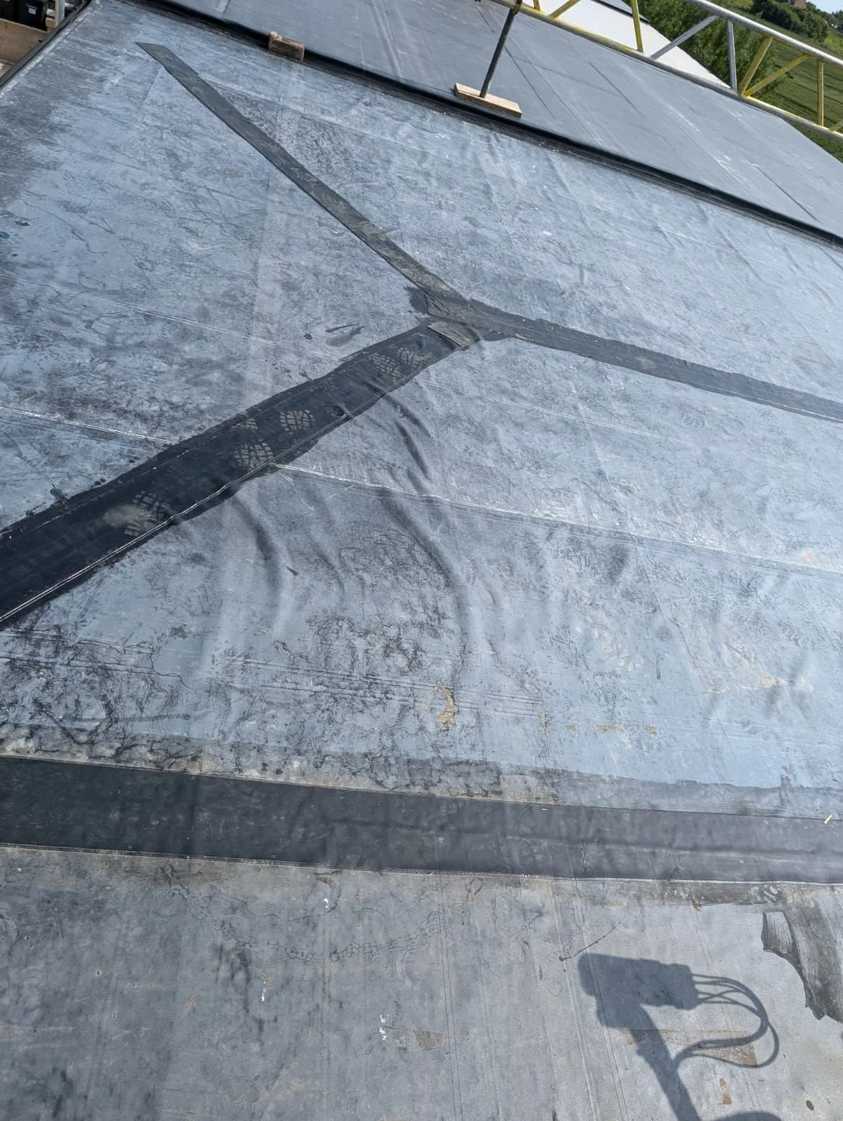 A compromised flat roof showing extensive bubbling, poor insulation layout, and severe surface wrinkling caused by failing liquid adhesives.