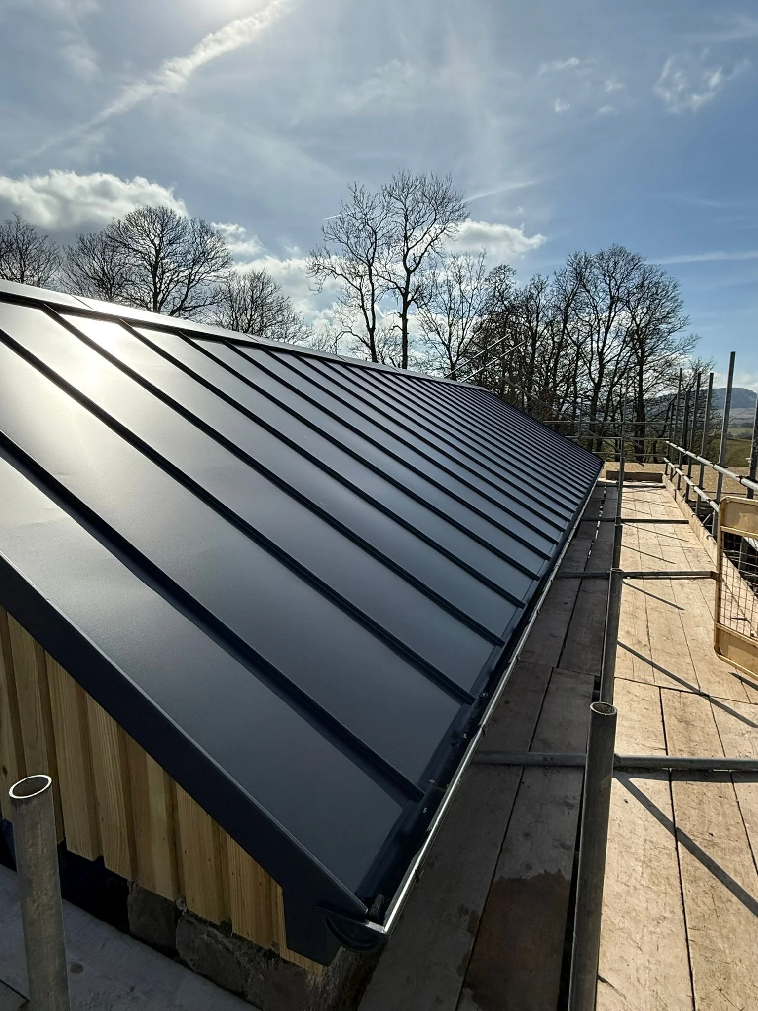 close-up perspective from the scaffolding platform, showcasing the impeccable surface finish, sharp corner details, and immaculate edge trimming that define ELAST’s premier metal roofing installations.
