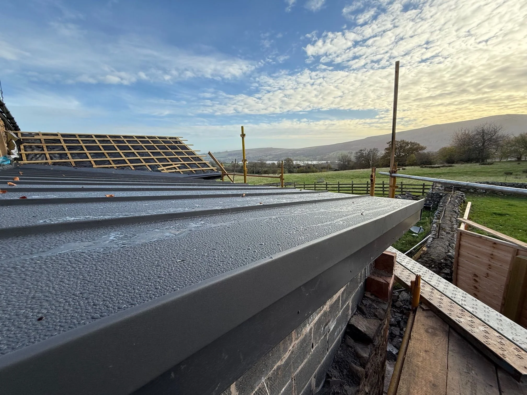 Clean, modern low-profile fascia and edge capping detail on a standing seam installation, perfectly framing the Cumbrian landscape.