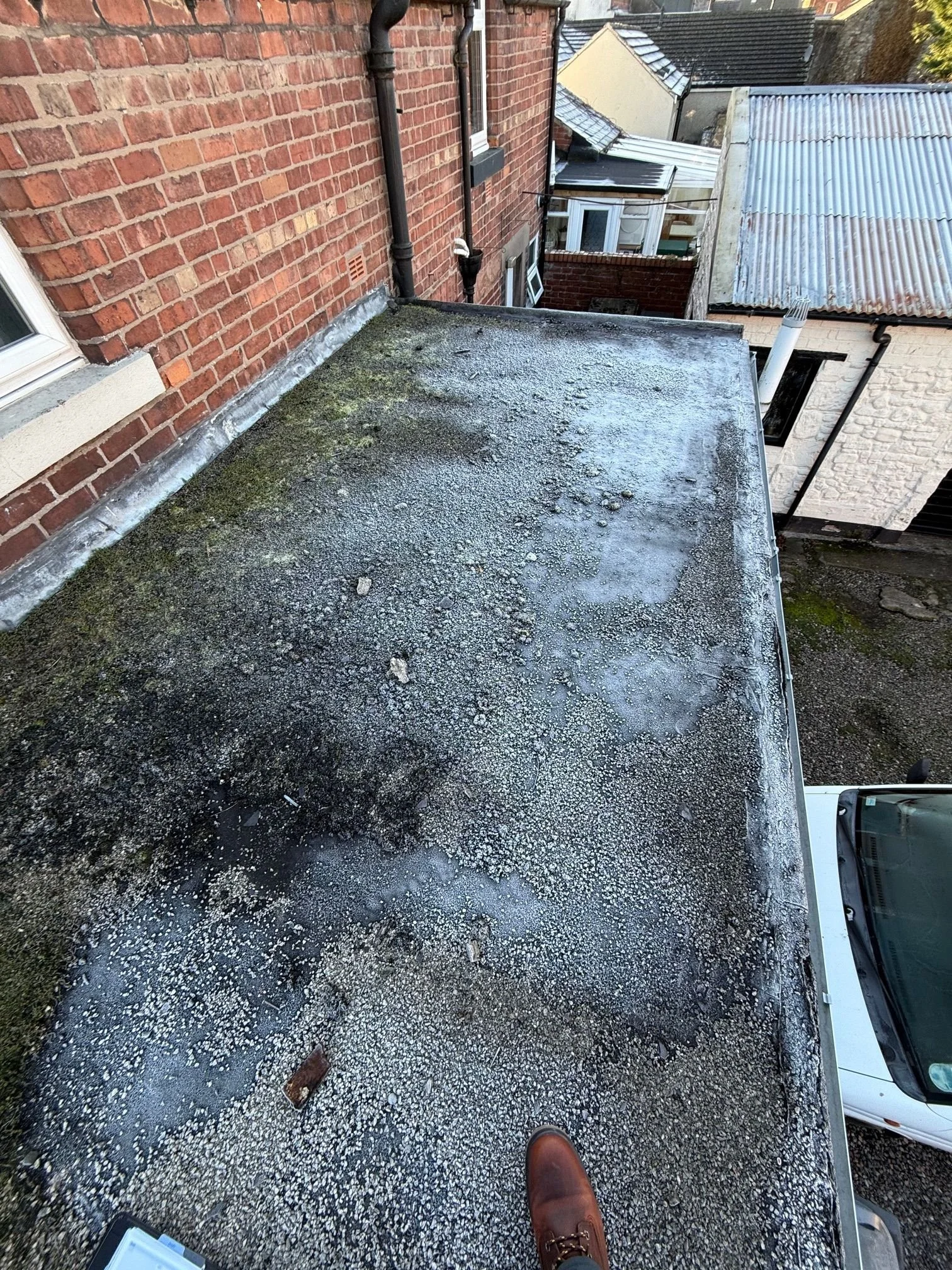 An aging, degraded flat roof covered in moss and gravel with visible signs of water pooling and surface failure.