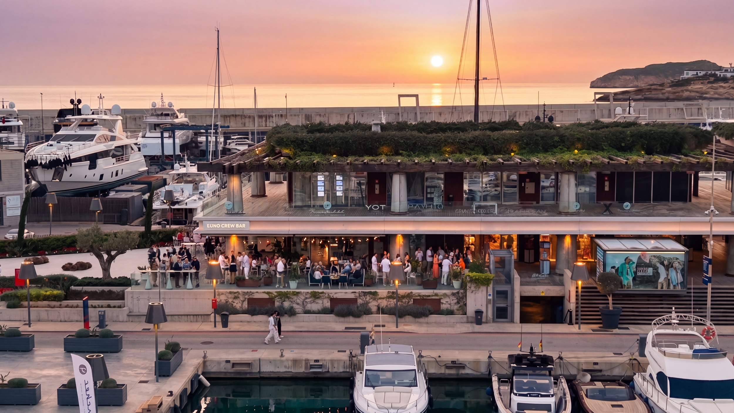 Sunset over a marina with yachts docked, a lively restaurant with people dining, and a hillside with modern buildings.