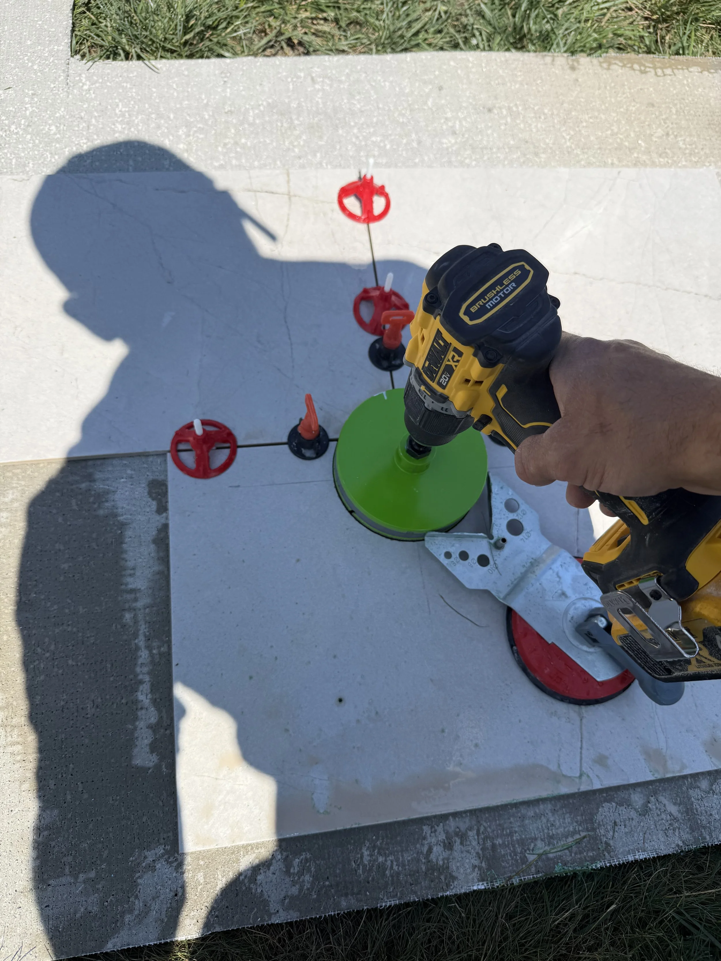 Person using a cordless drill to secure a green tripod on a concrete surface with red- and black-colored leveling tools nearby.