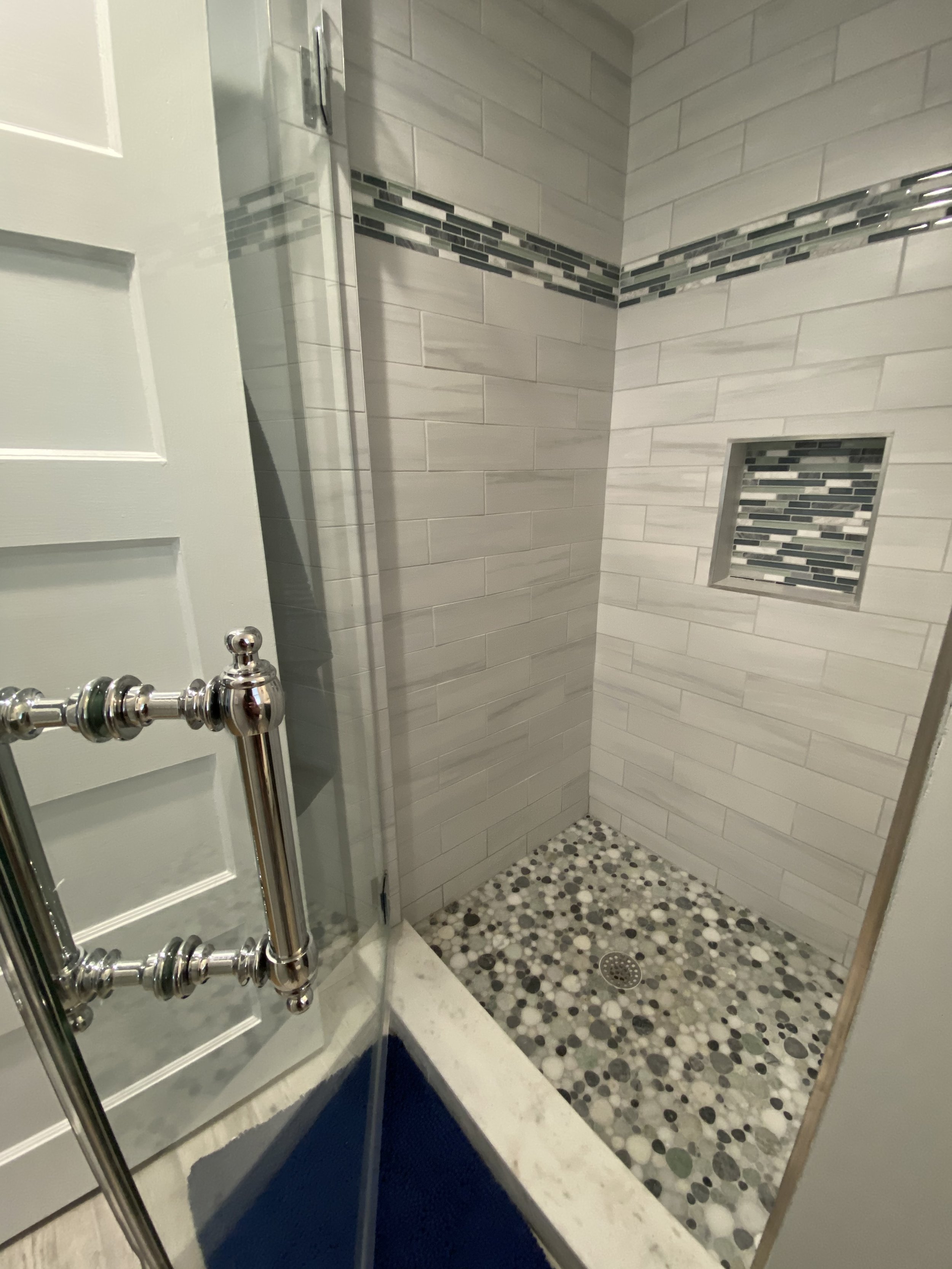 A walk-in shower with tiled walls, a built-in niche, and pebble tile flooring in neutral tones.