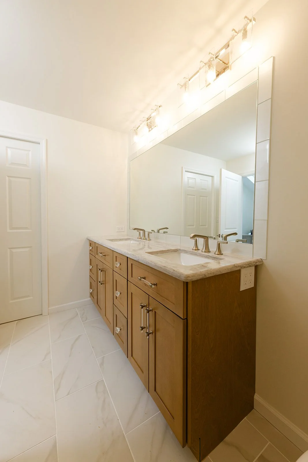Bathroom with double vanity, marble countertop, large mirror, and modern gold fixtures.