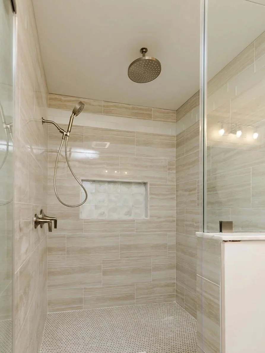 Bathroom shower with a rain showerhead on the ceiling and a hand-held showerhead on the wall, beige tile walls, small mosaic tile floor, built-in niche with stone tiles.