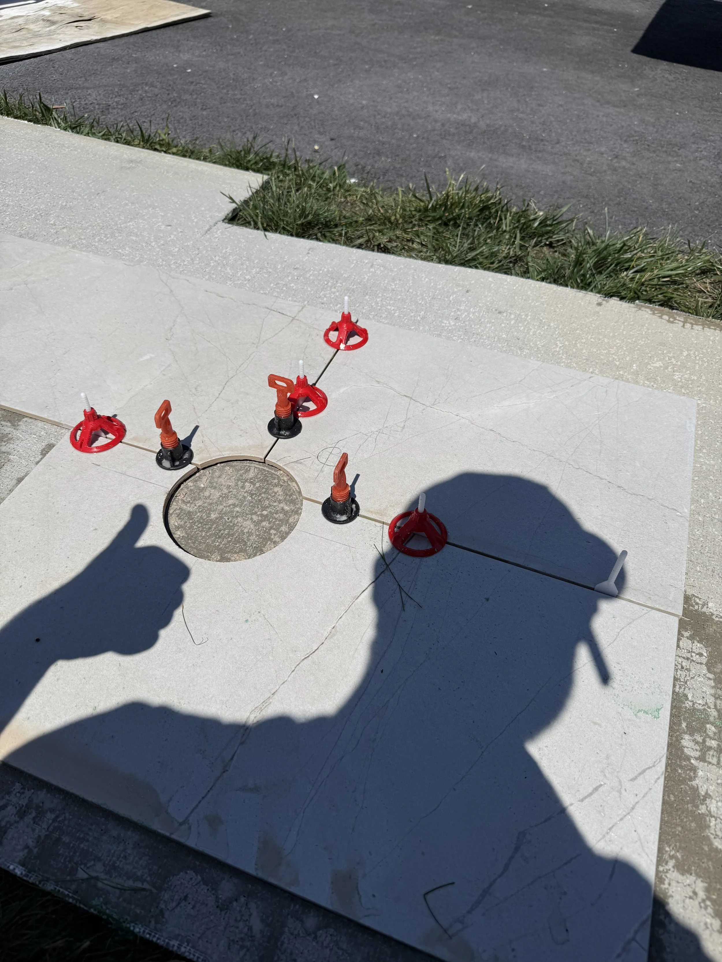 Covering with a white tile a manhole and with red and black temporary barriers. A shadow of a person is visible on the tile surface.