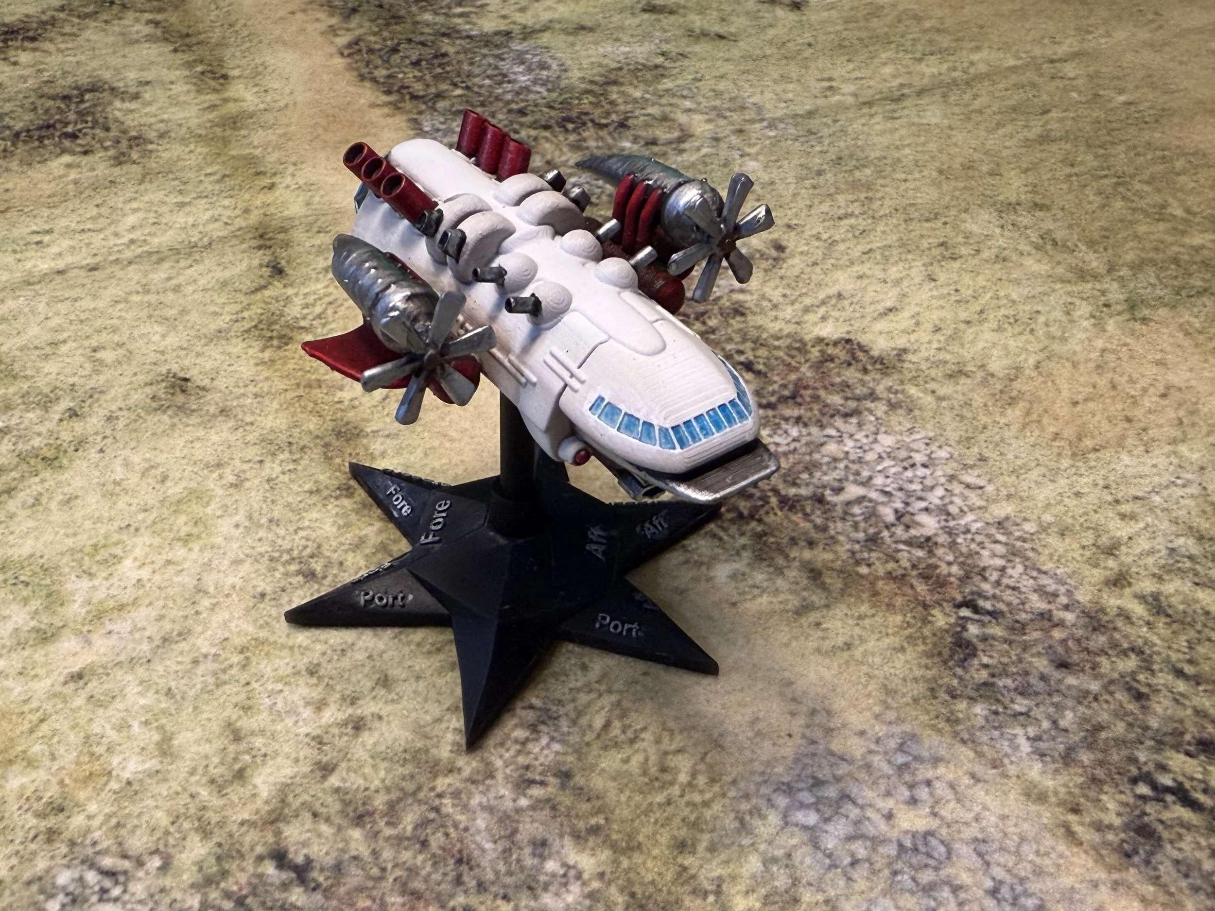 A model spaceship on a stand with the word 'Port' written on the base, set against a textured yellow and brown surface.