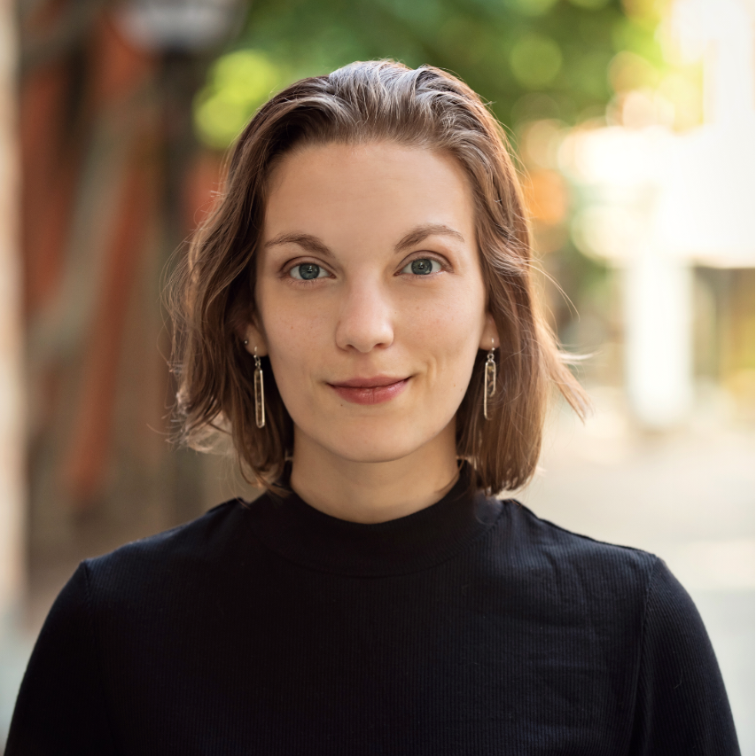 Headshot of smiling female tutor with long curly brown hair wearing a lanyard.