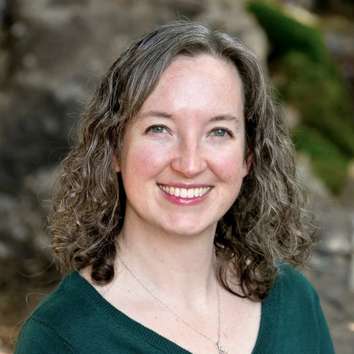 Headshot of smiling female tutor with long curly brown hair wearing a lanyard.