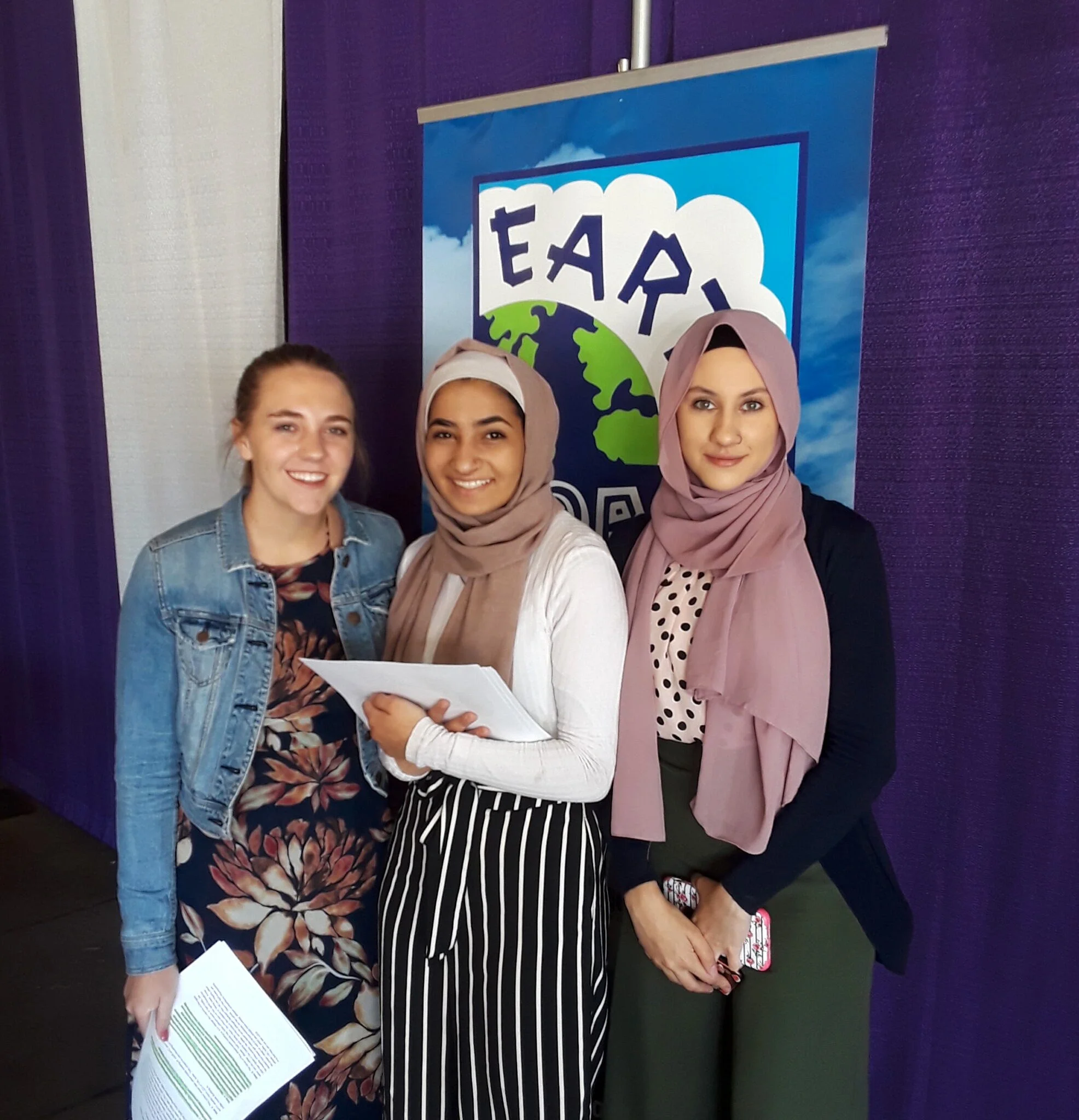 Three students posing together in front of a banner