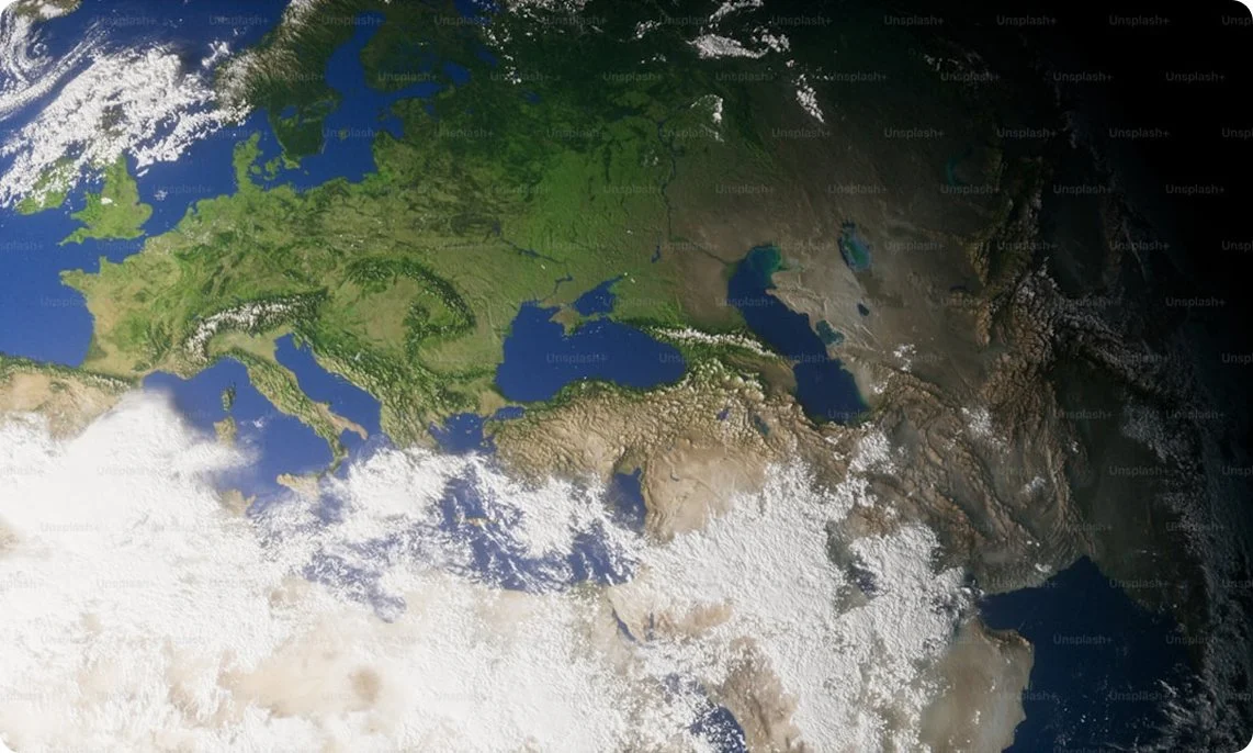 A satellite view of Europe, Asia, and parts of Africa showing landmasses with mountains, forests, and bodies of water, with cloud cover over some regions.