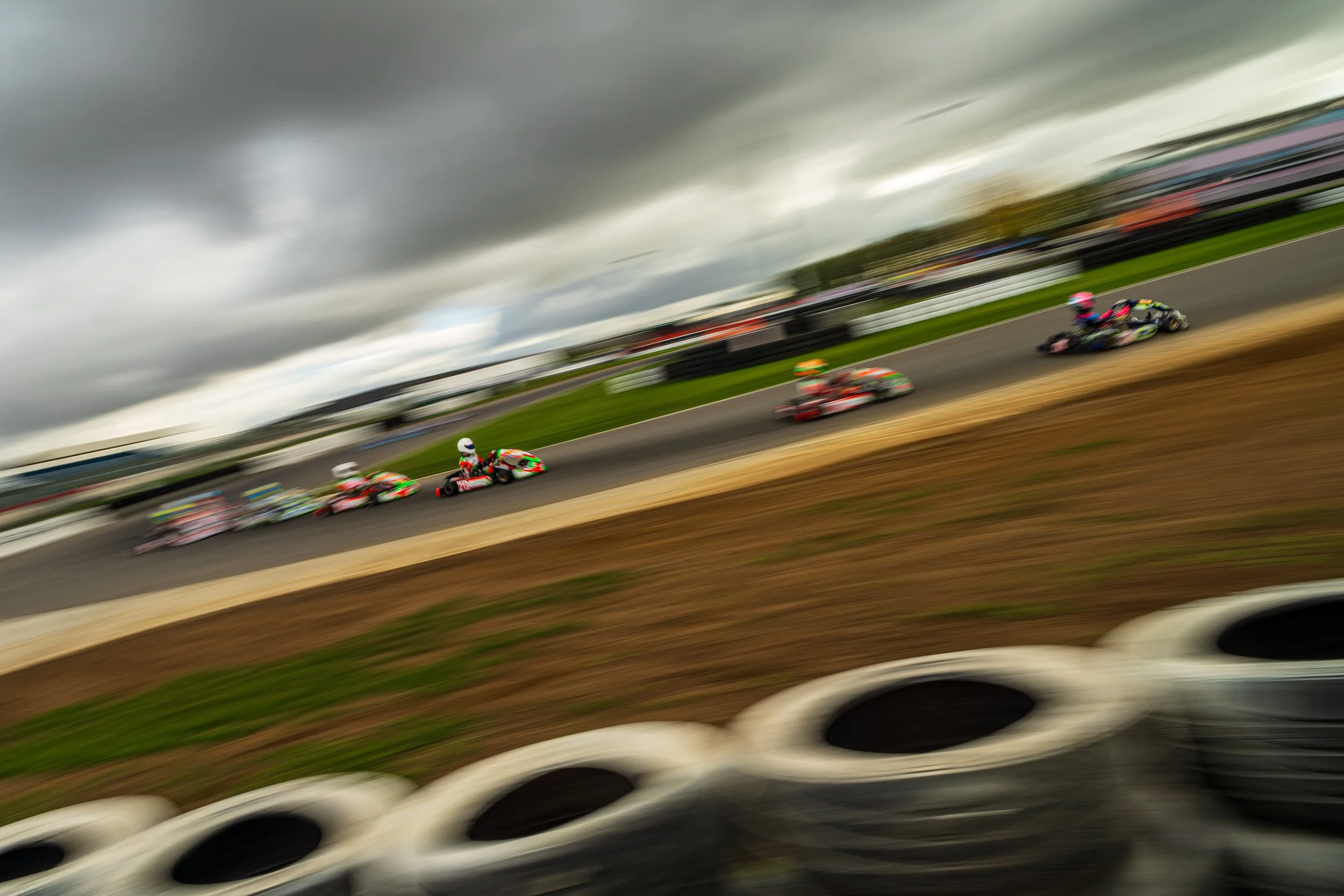 Wide view of kart racing beneath a dramatic sky at Silverstone.