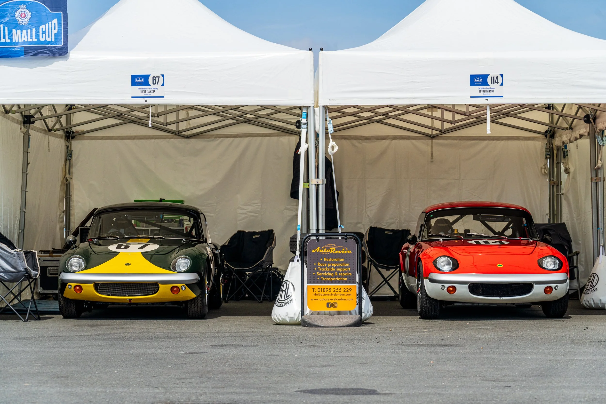 Colourful classic sports cars beneath paddock awnings at Donington Historic Festival.