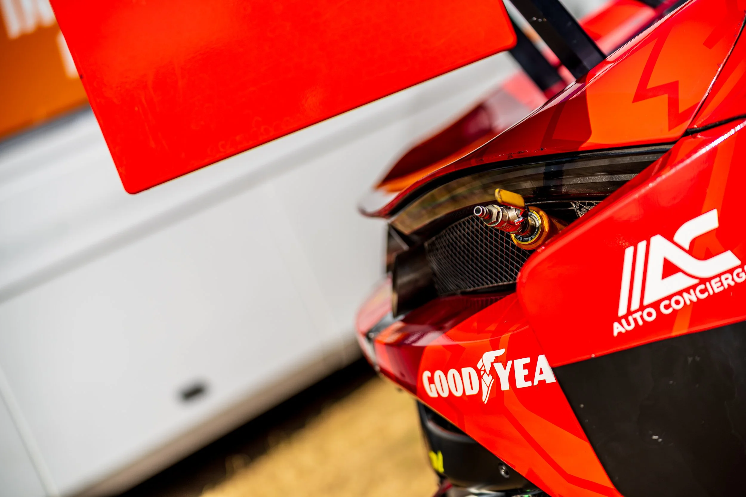 Close-up of a red race car with sponsor decals, including Goodyear, showing its front side with a visible headlight and a part of the hood.