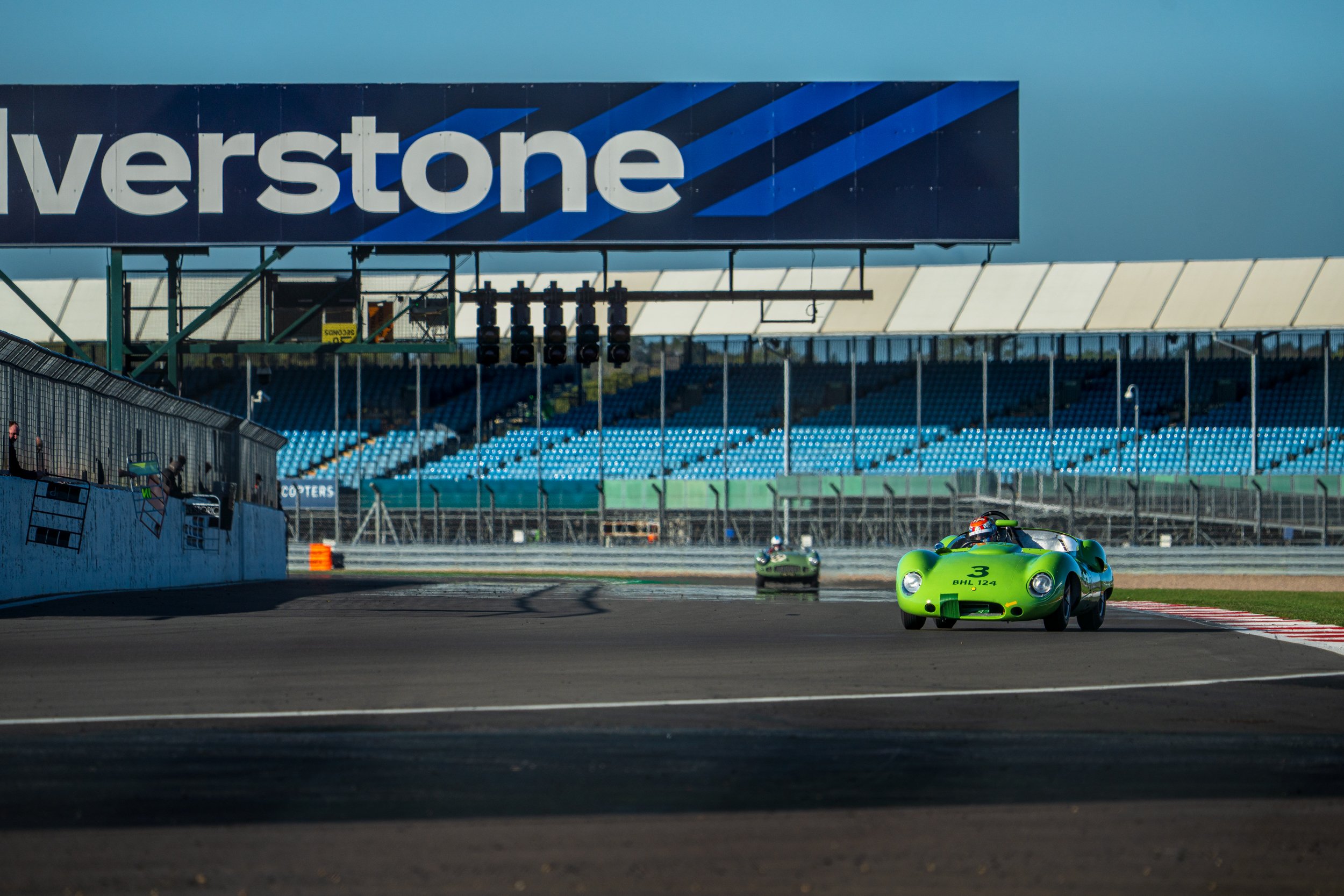 Green racing car passing the Silverstone sign and grandstand.