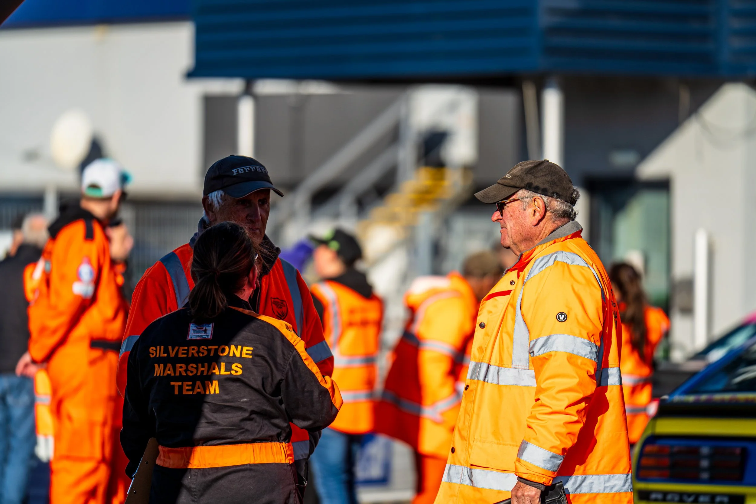 Marshals in orange overalls talking in the Silverstone paddock.