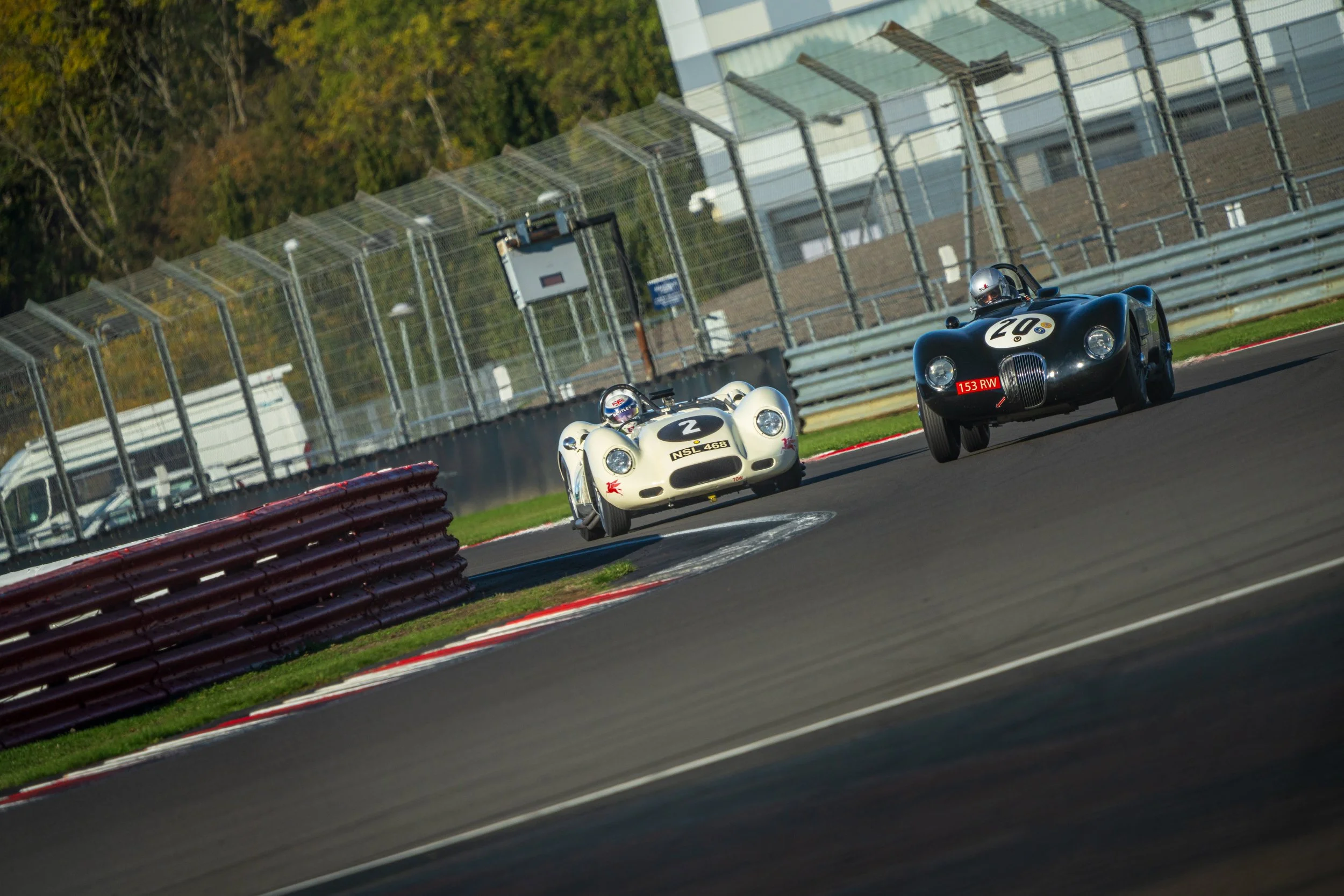Cream classic saloon leading a group of cars around the Silverstone circuit.