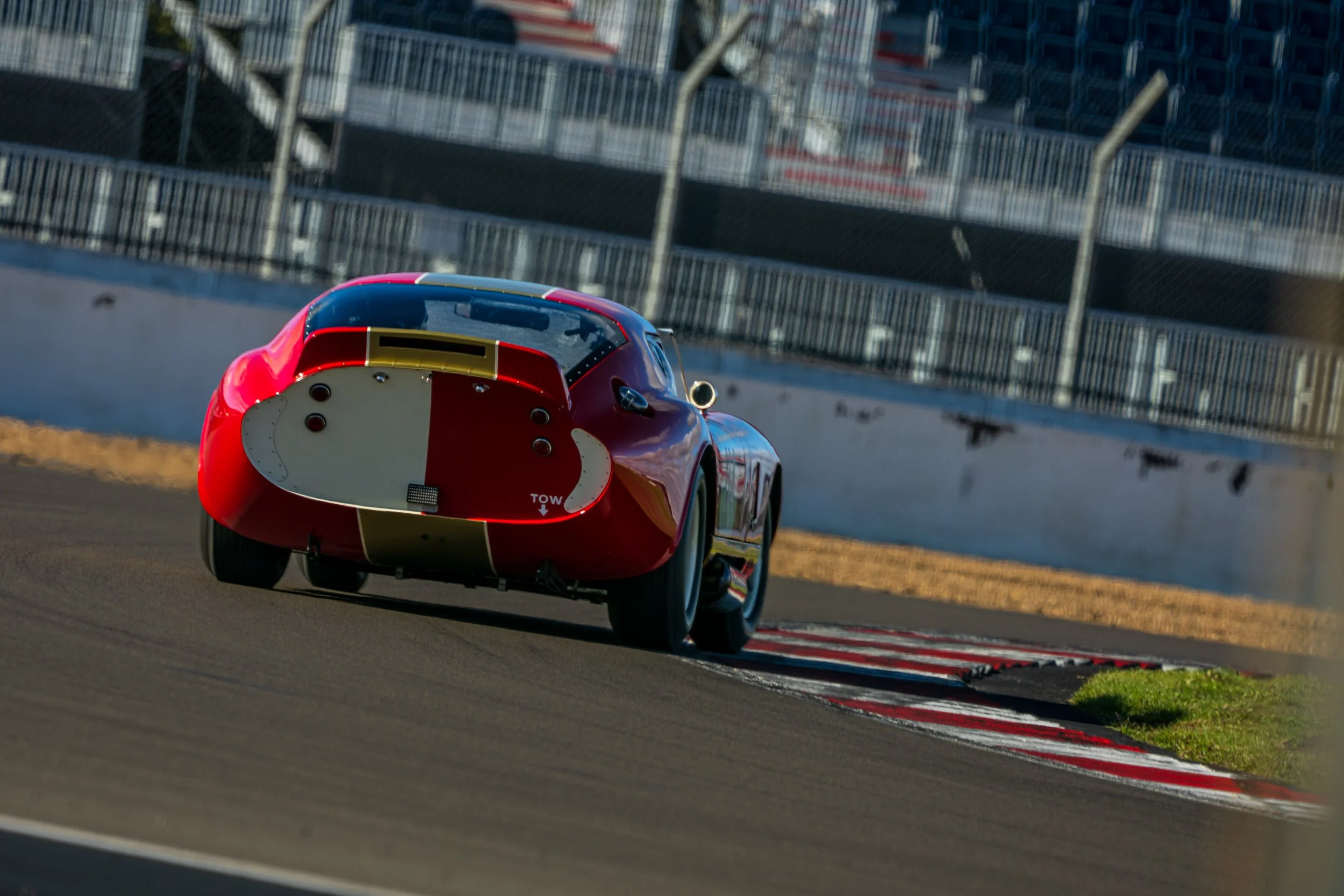 Rear view of a red classic sports car taking a corner at Silverstone.