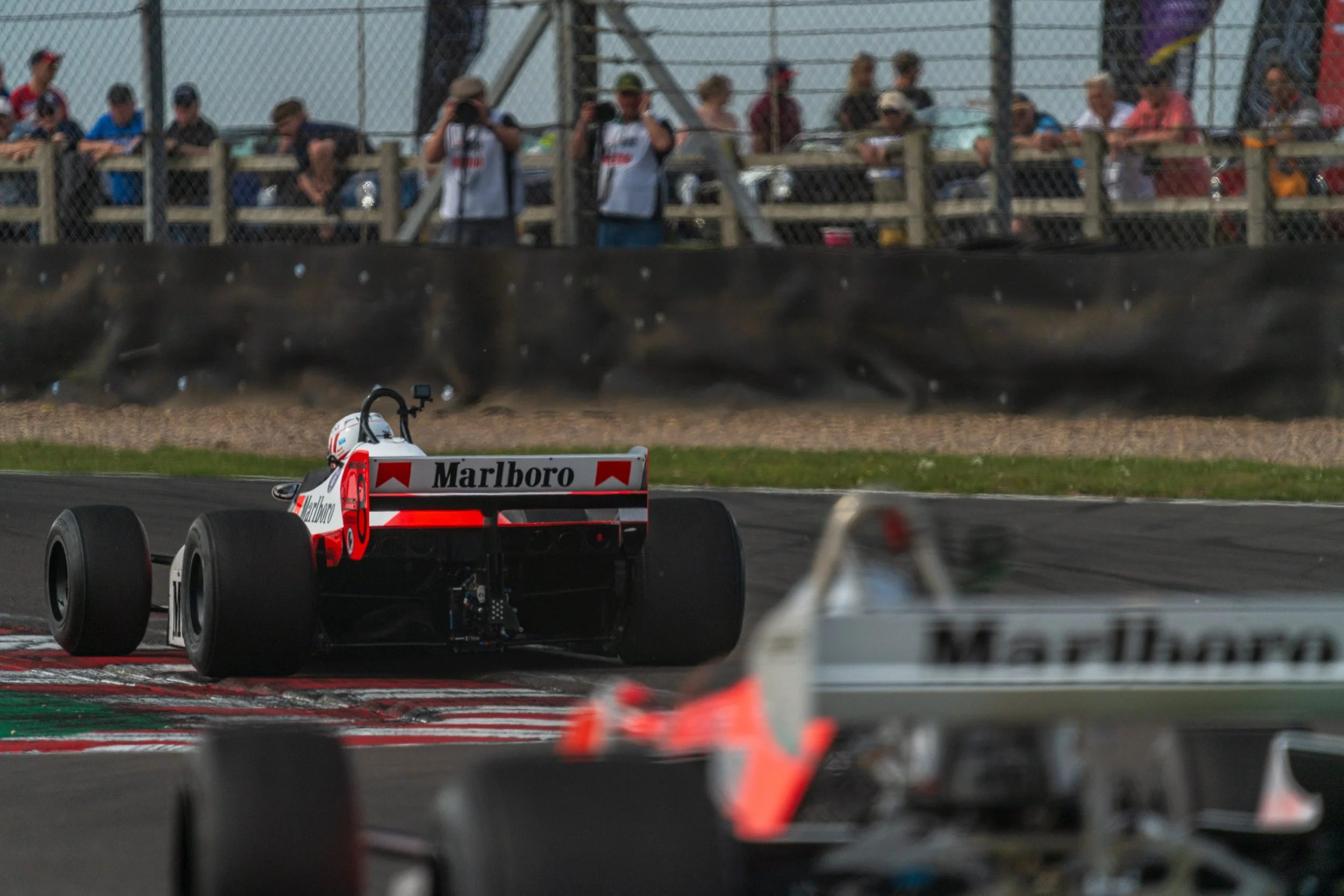 Rear of a racing car in the Donington pit lane, with spectators watching from above.