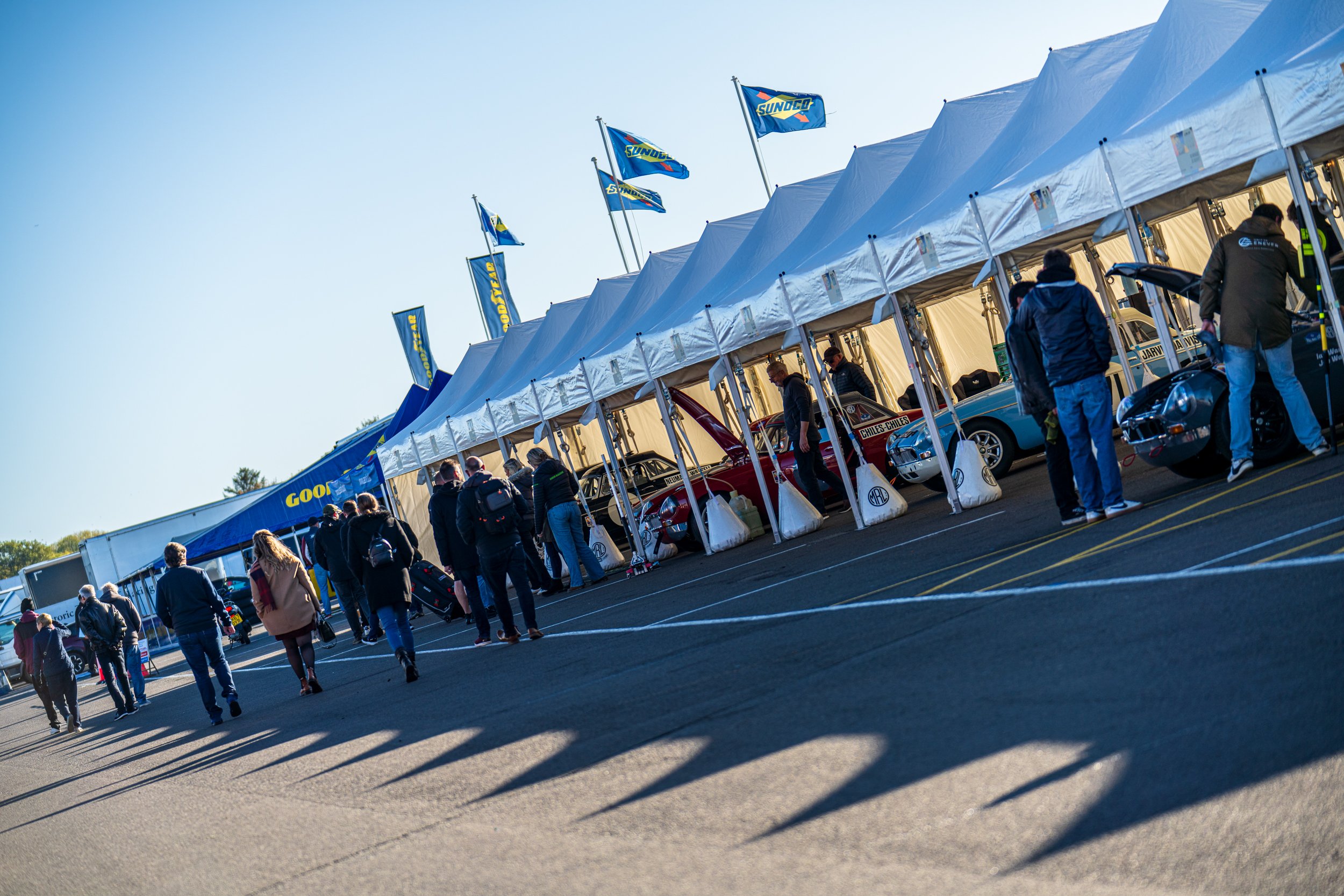 People gathered beside event tents and flags in the Silverstone paddock.