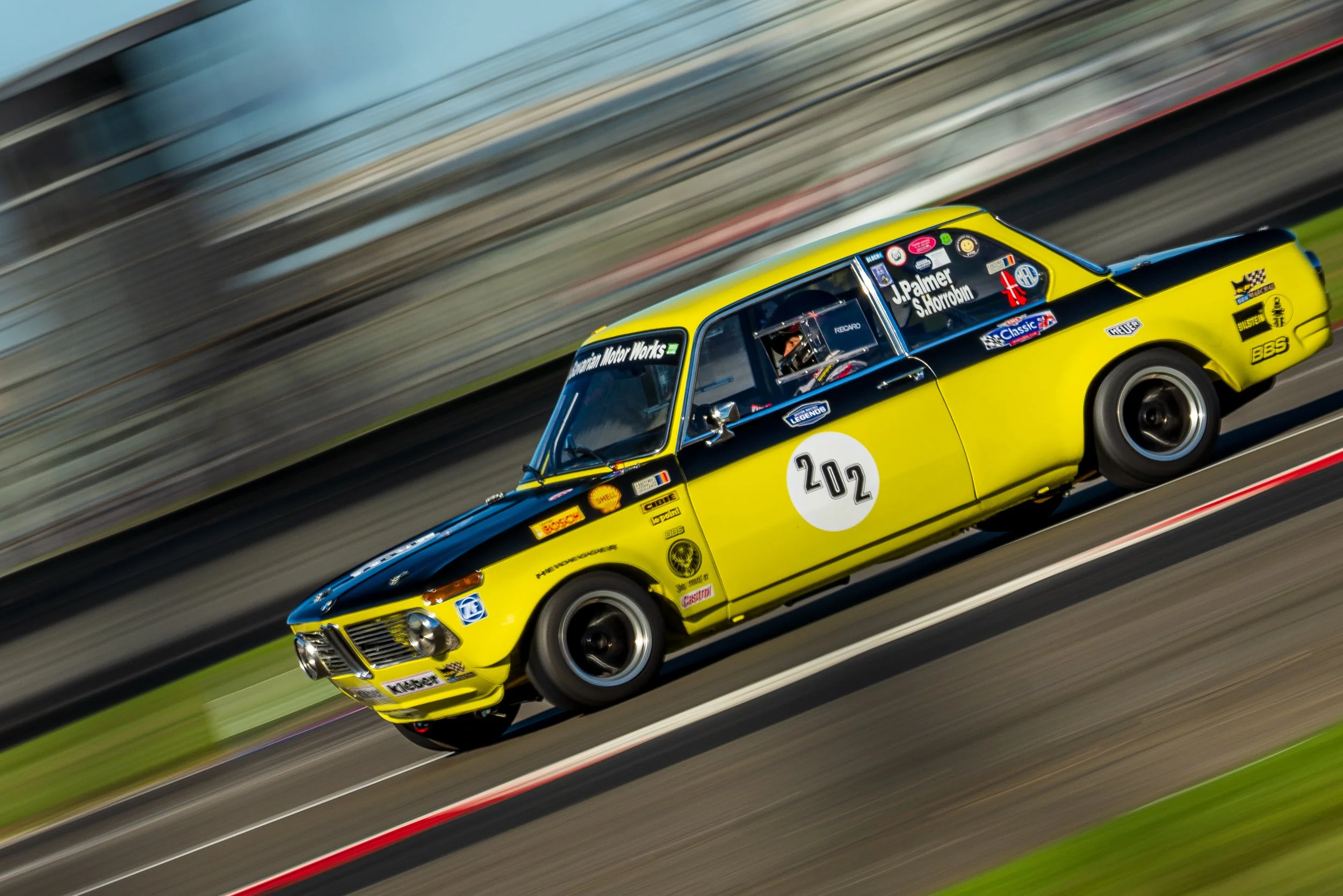 Yellow classic saloon racing car captured at speed at Silverstone.