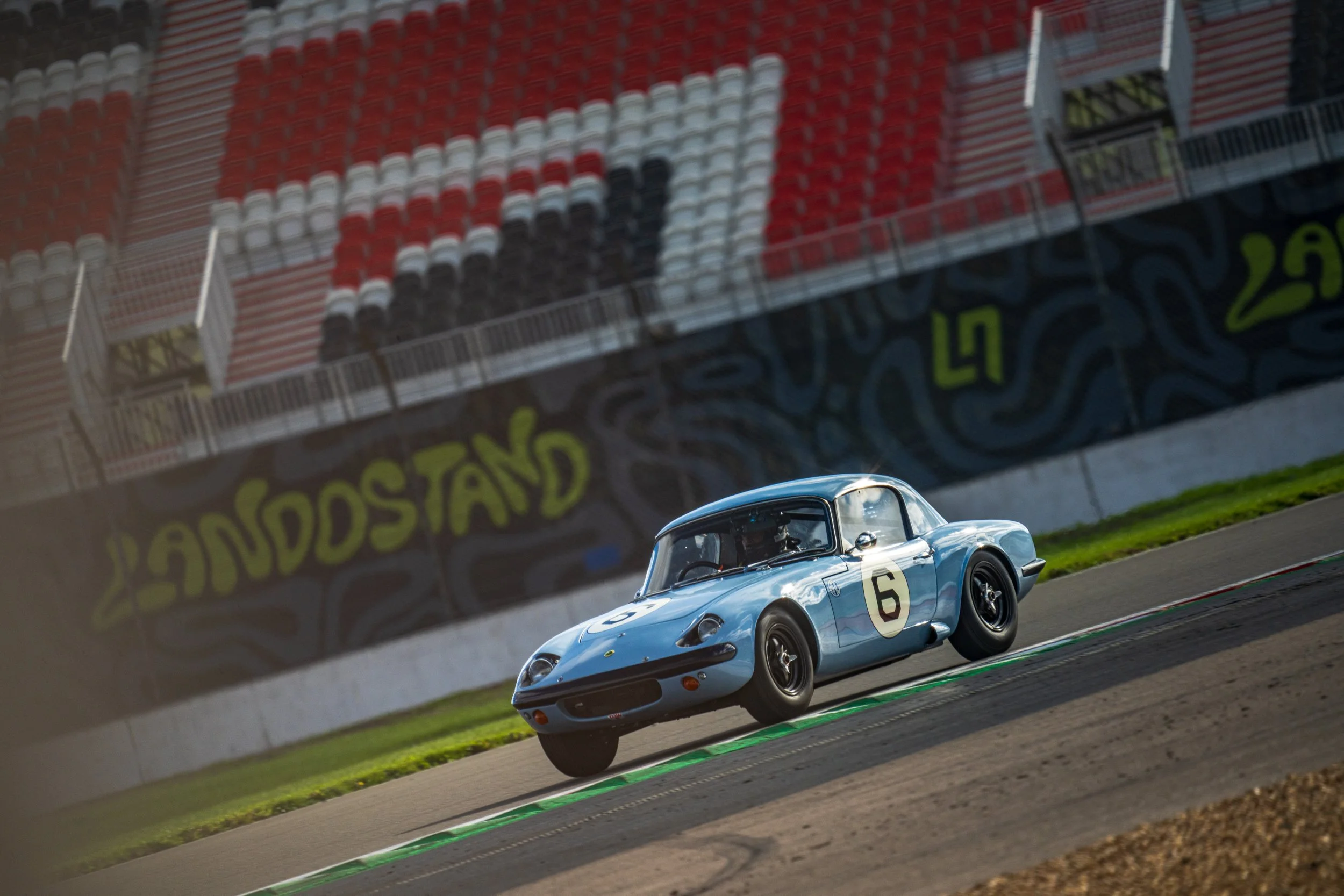 Light blue classic sports car racing beside a kerb at Silverstone.