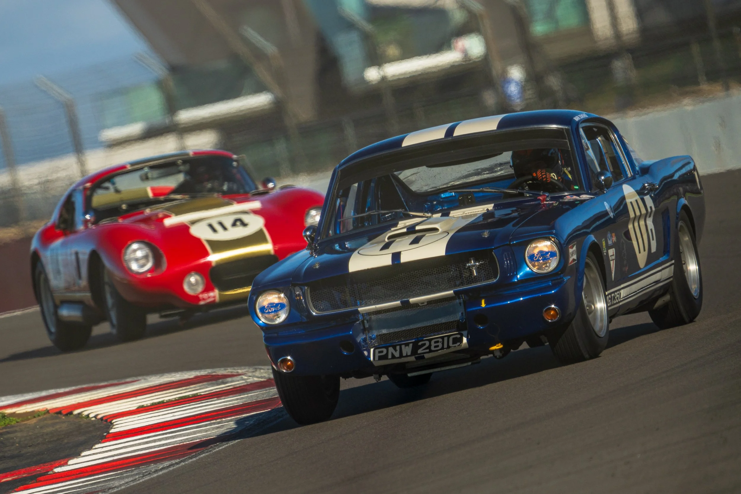 Blue and white classic sports car clipping a kerb at Silverstone.