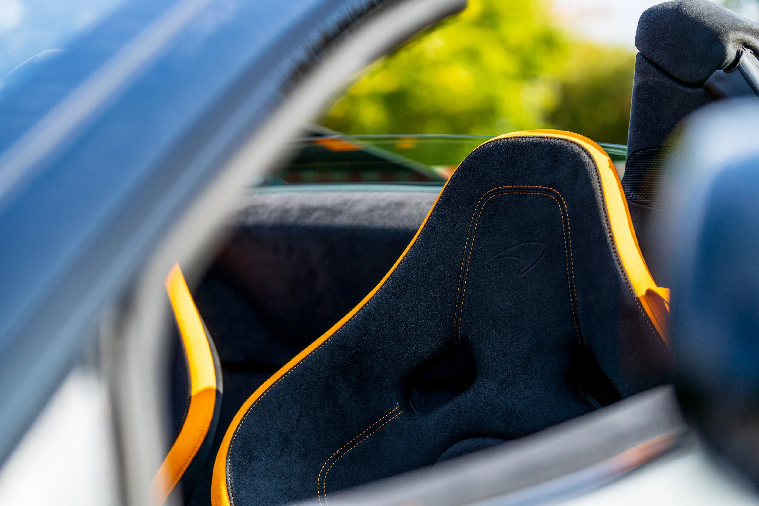 View inside a car showing a black and yellow racing seat with a headrest and a green landscape outside the windows.
