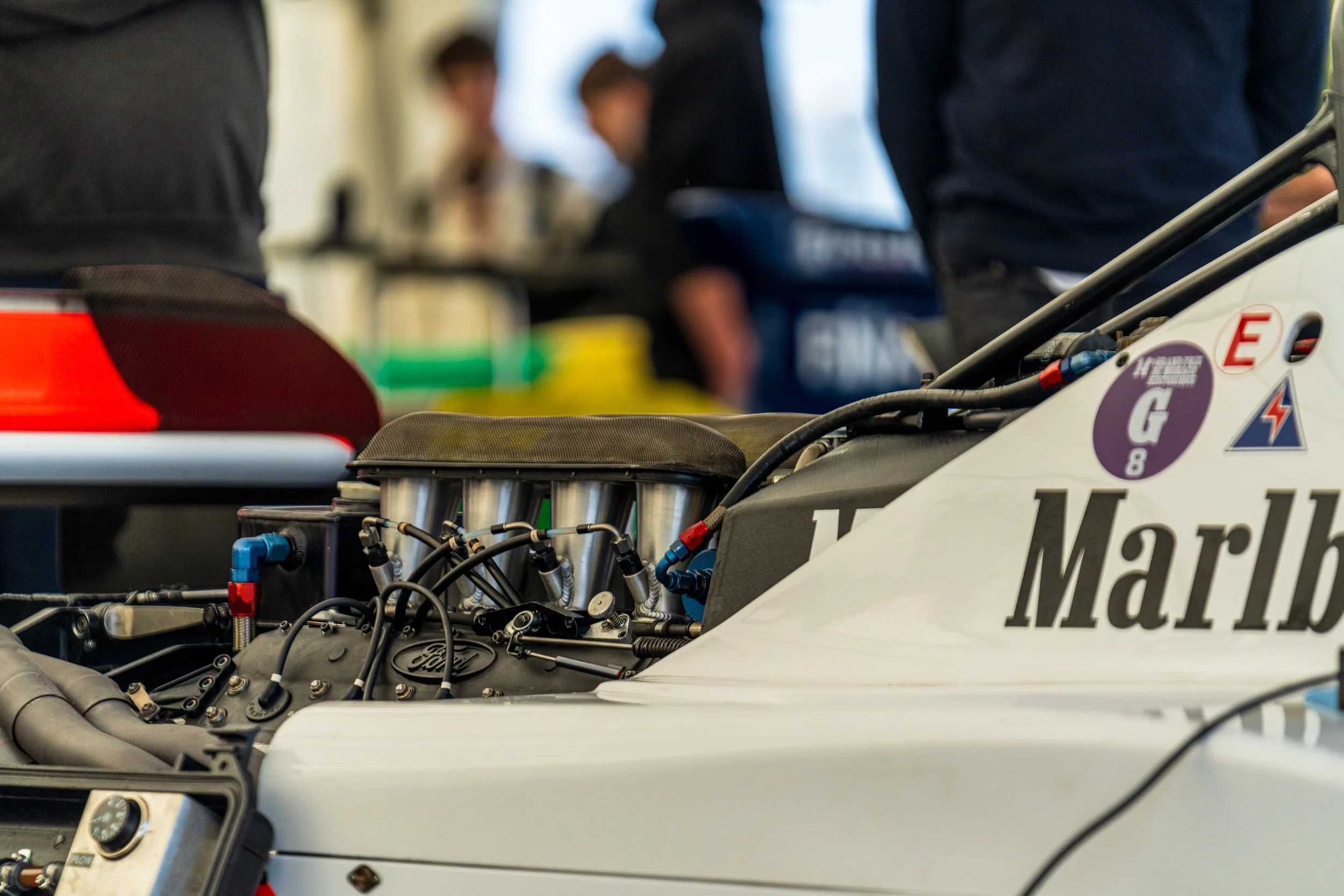 Mechanical detail of a cream racing car with people working in the Donington paddock.