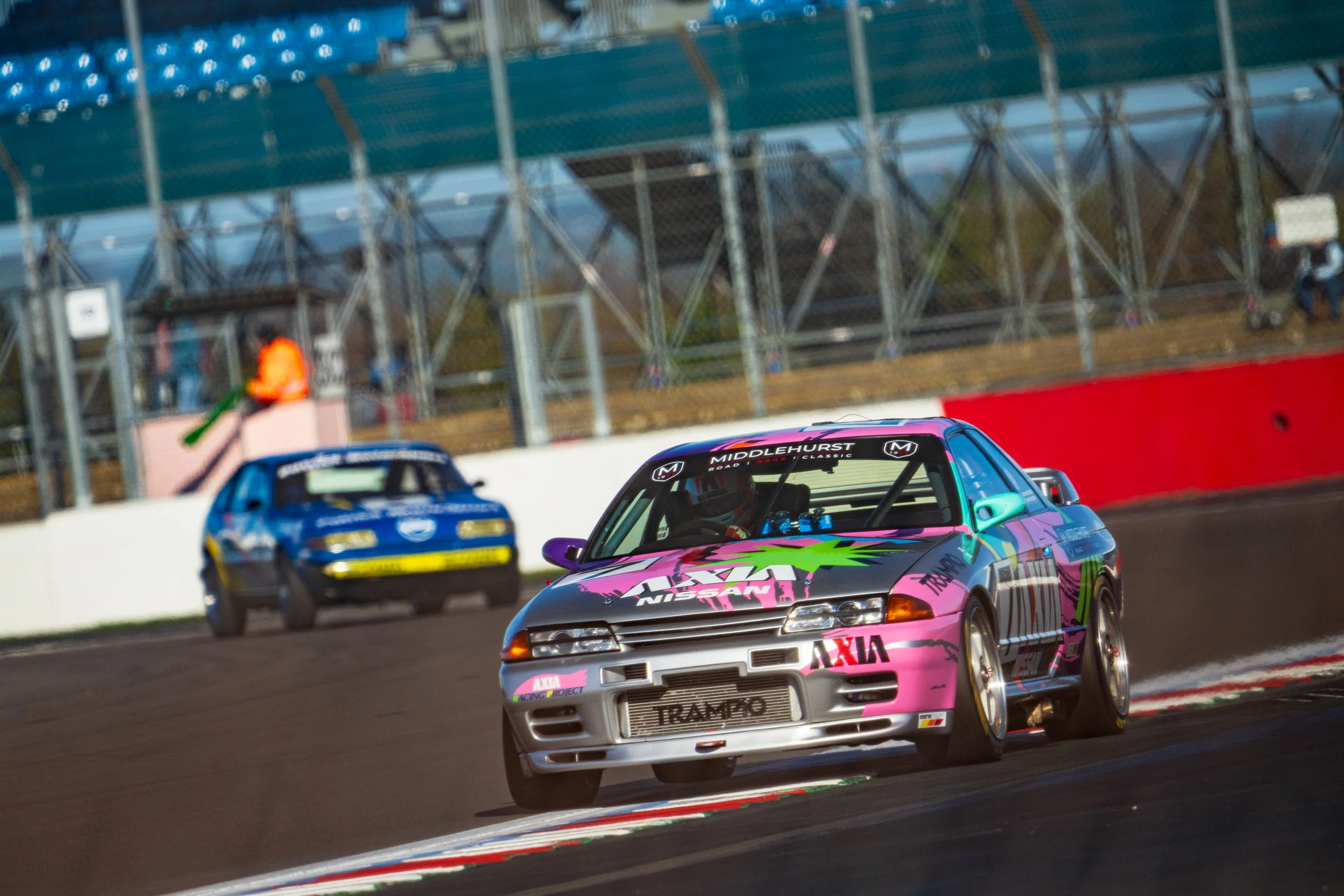 Pink and black touring car racing at Silverstone, with blue cars behind.