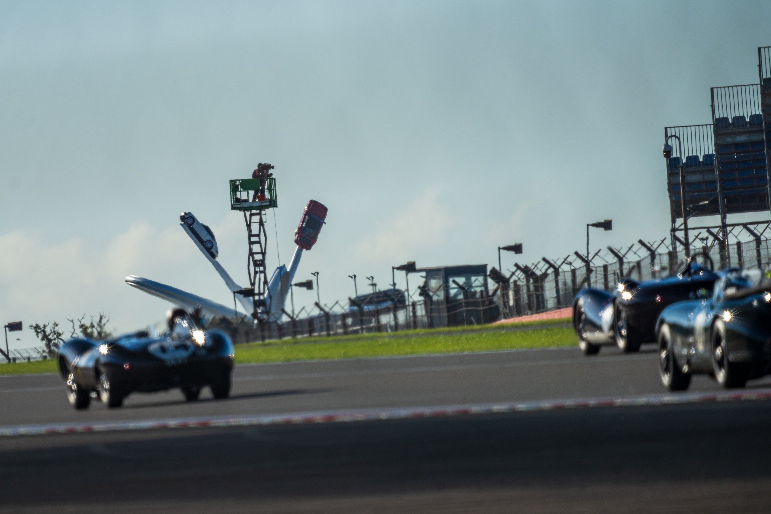 Racing cars on the Silverstone circuit with a large sculpture visible in the distance.