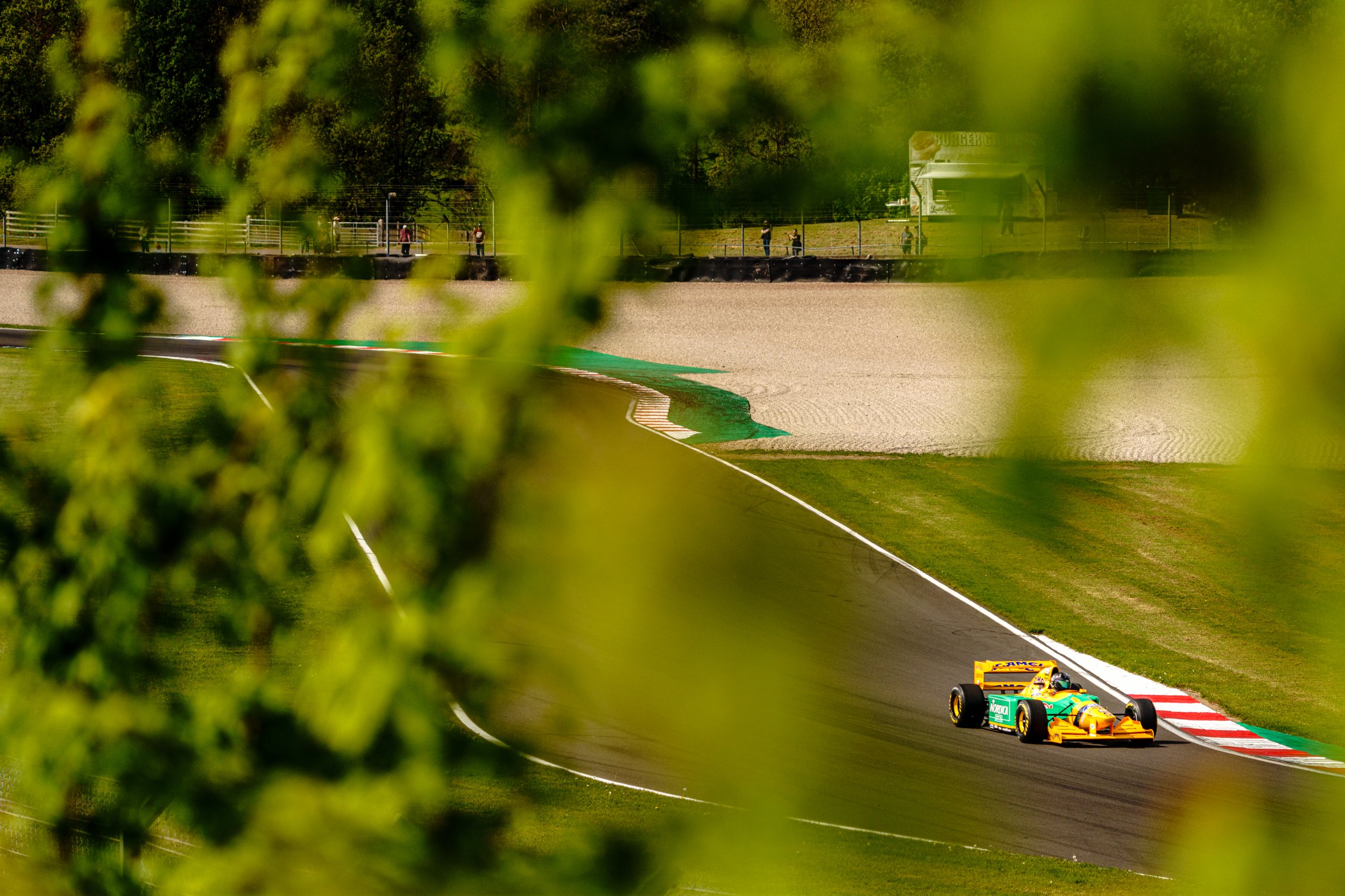 A racing car seen through green foliage beside the Donington Park circuit.