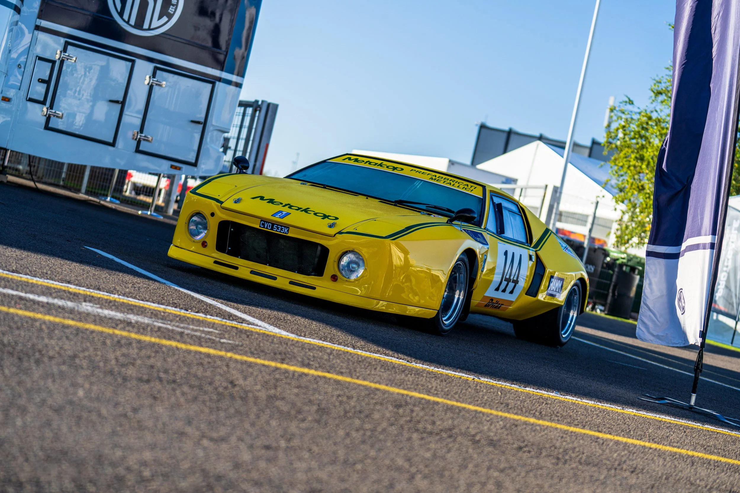 Yellow classic racing car parked in the Silverstone paddock.