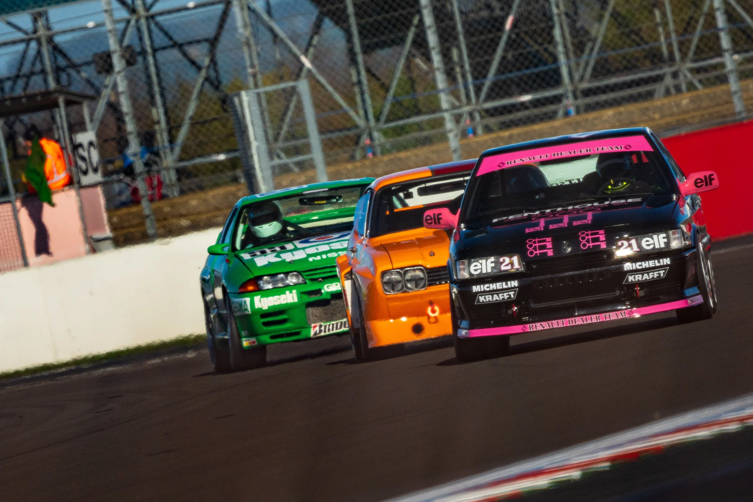 Black, orange and green touring cars racing closely together at Silverstone.