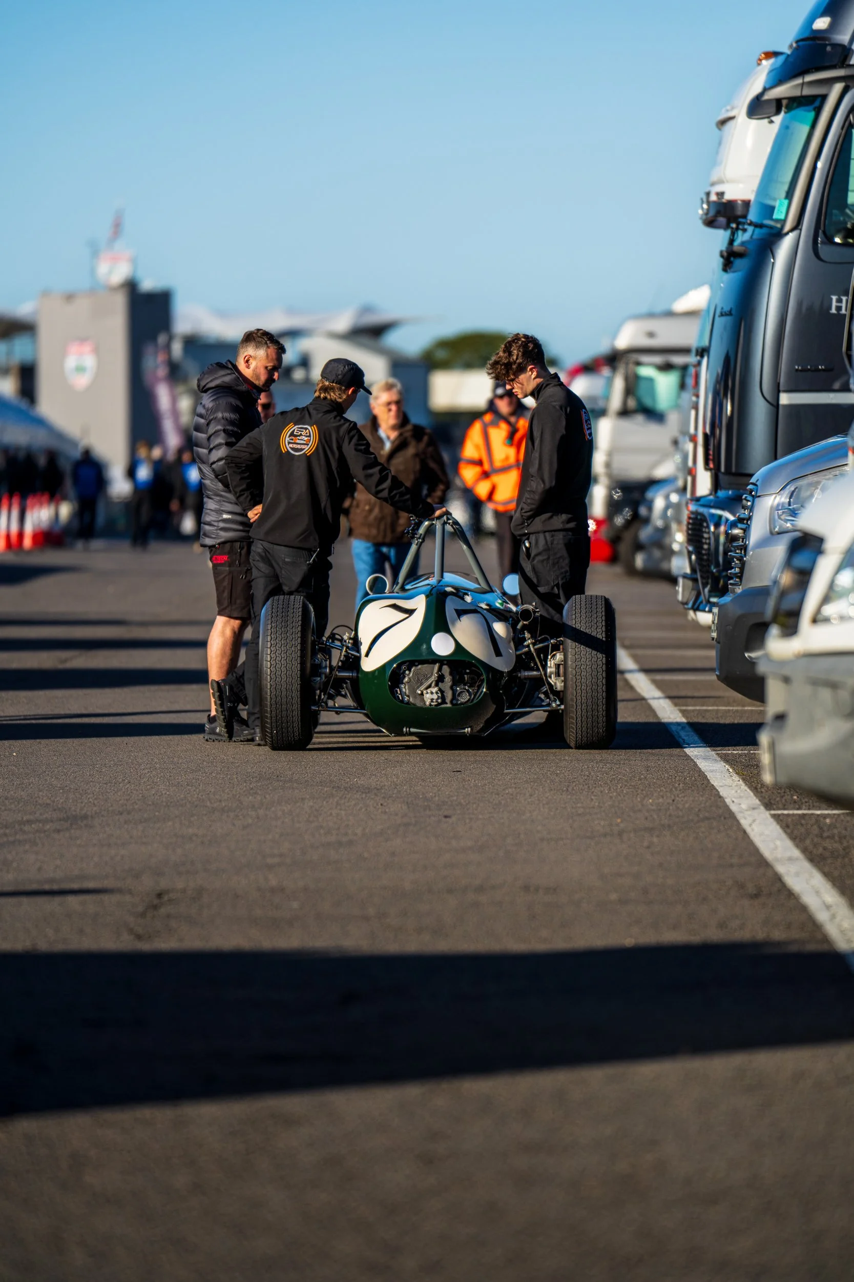 Team members pushing a green single-seater through the Silverstone paddock.