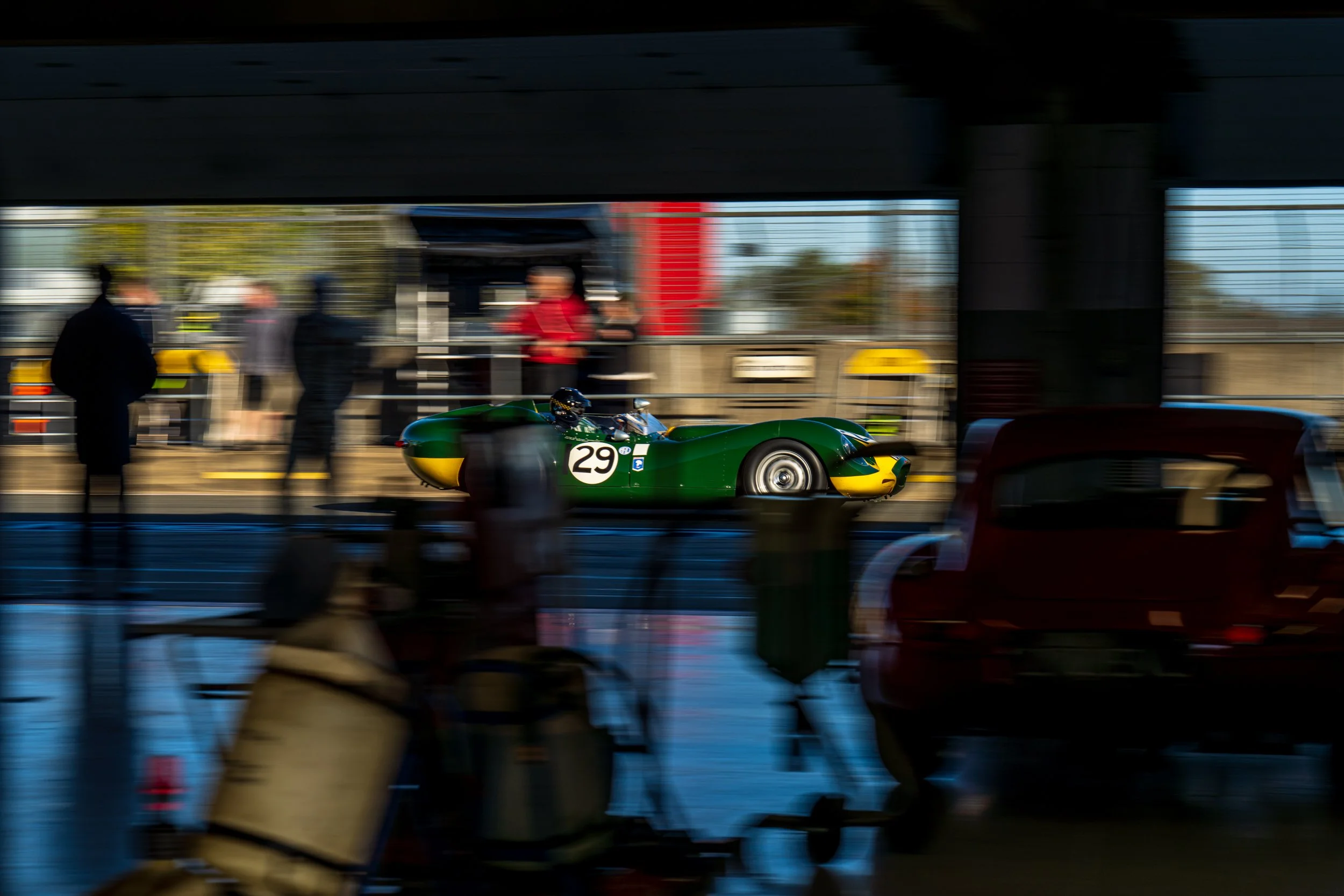 A racing car and blurred team activity seen inside a Silverstone pit garage.