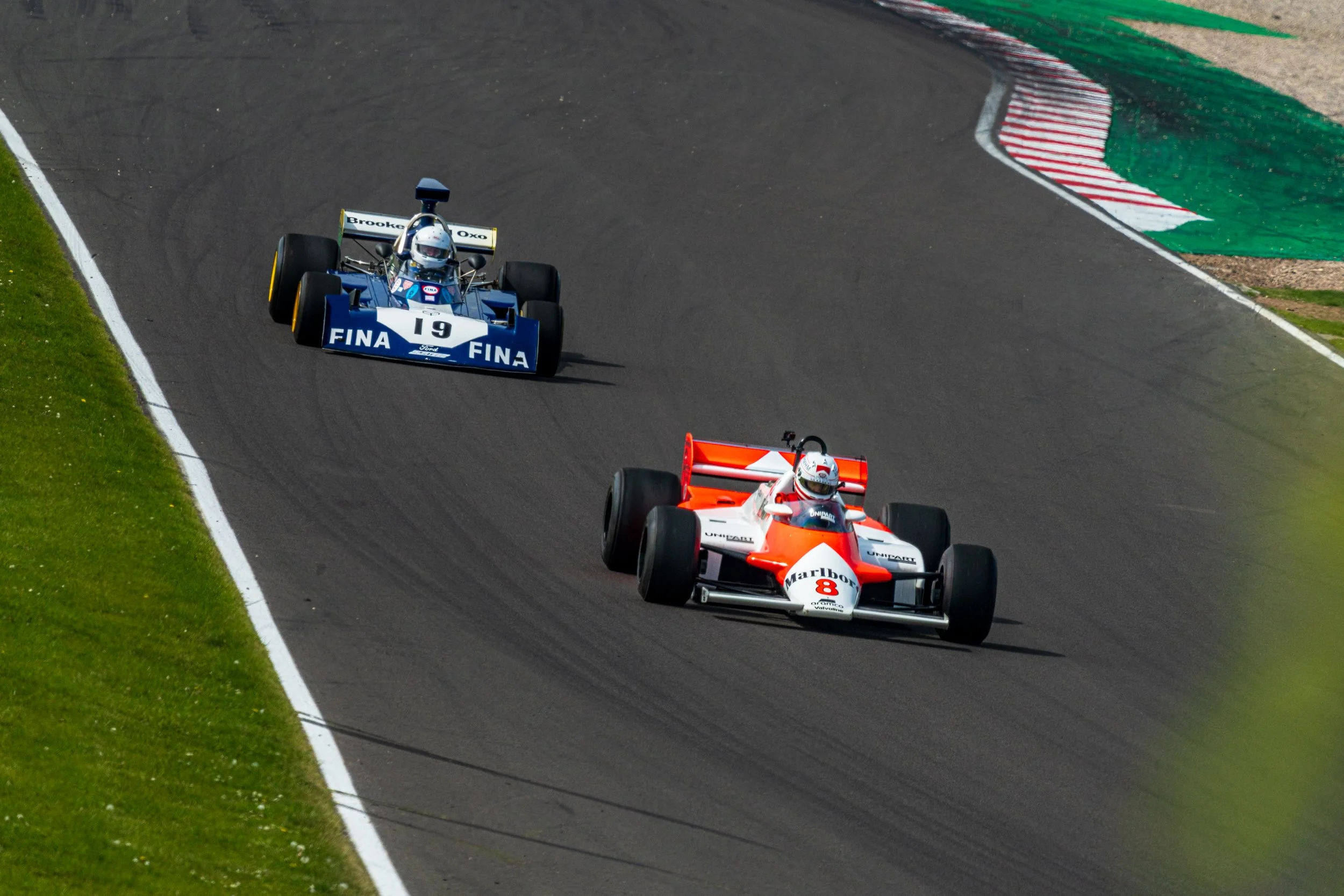 Orange and white single-seater followed by a blue racing car at Donington Park.