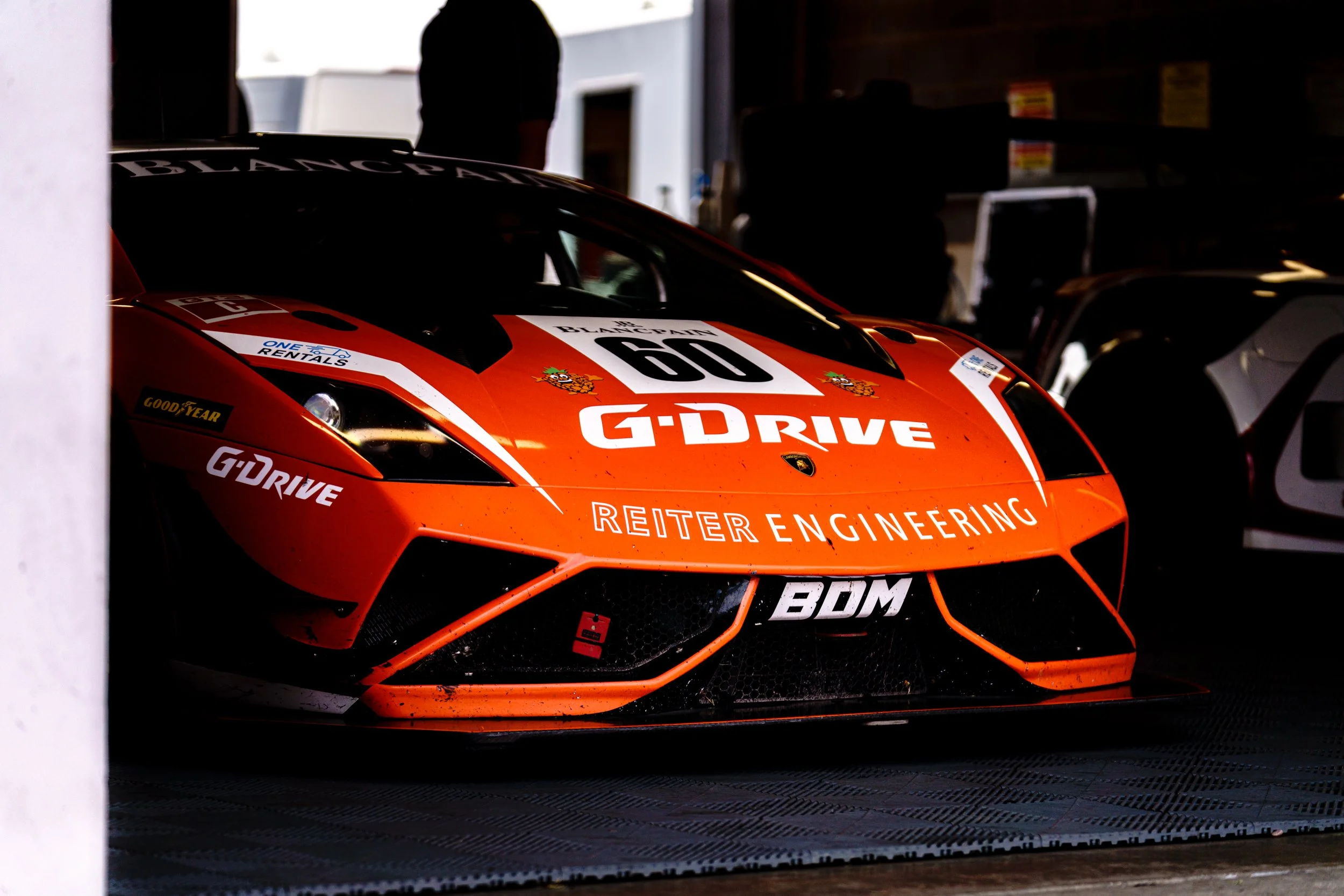 Orange GT racing car in a pit garage at Donington Historic Festival.