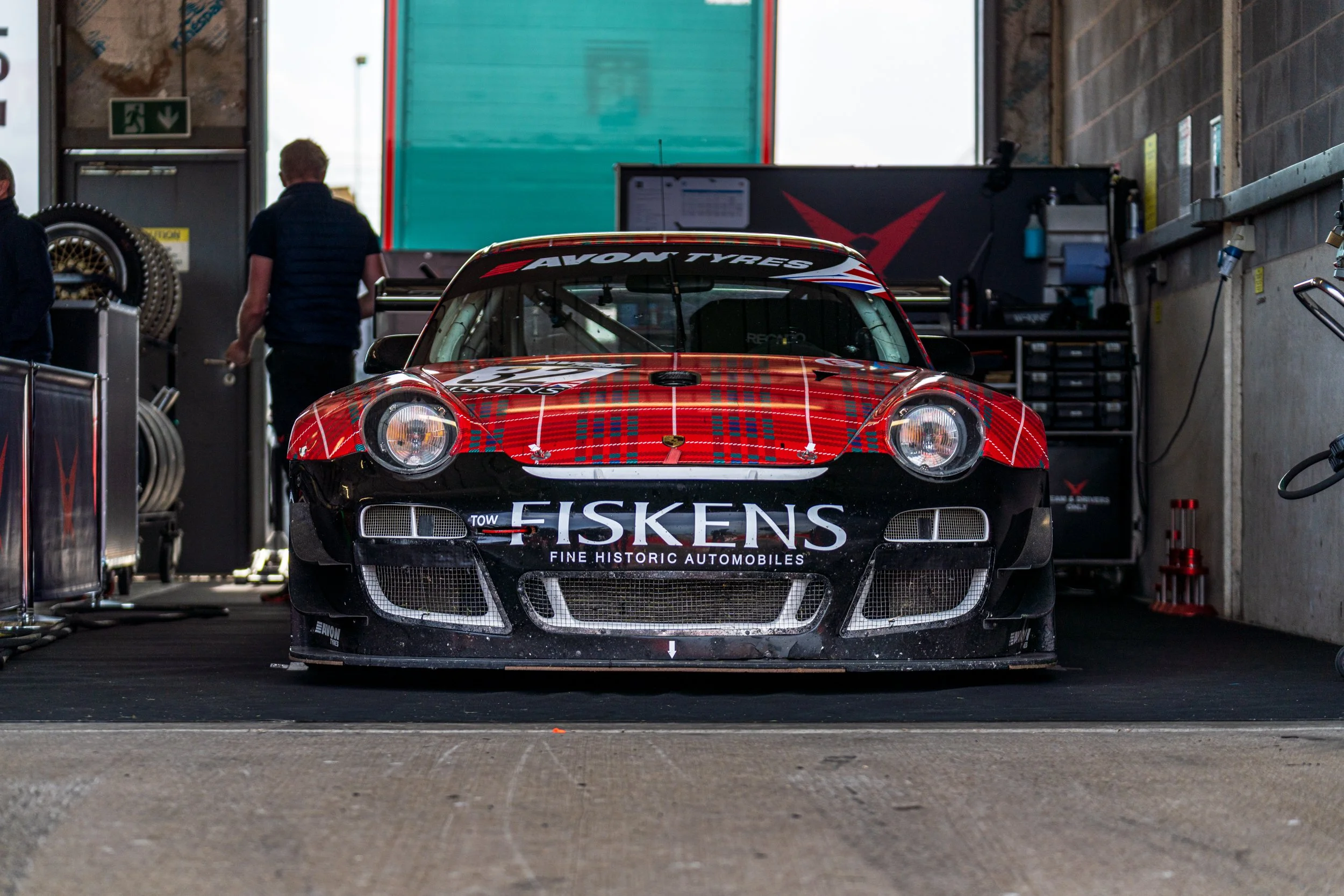 Front of a red and black classic Jaguar racing car inside a Donington pit garage.