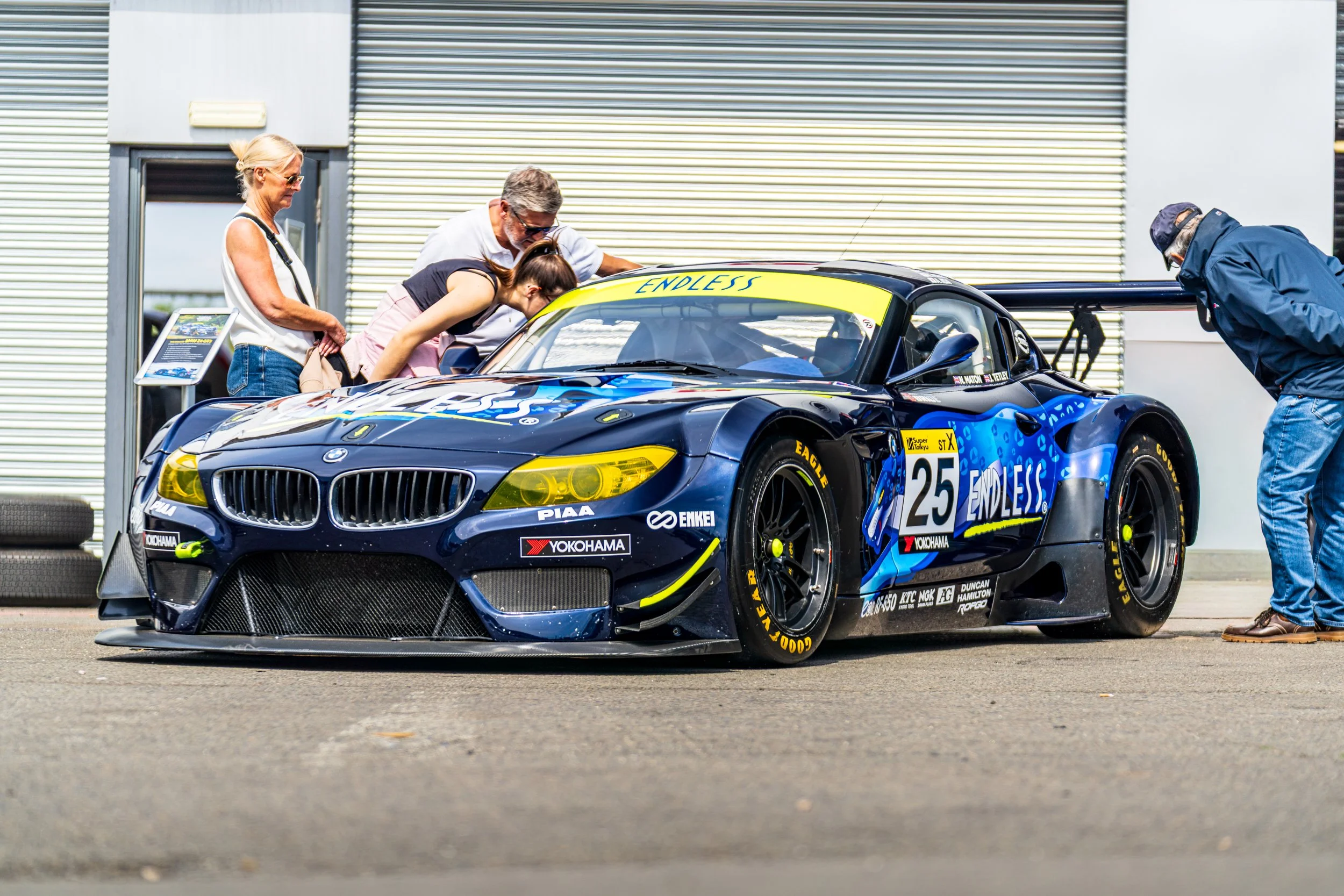 Blue and yellow GT racing car being attended to in a Donington Park pit garage.