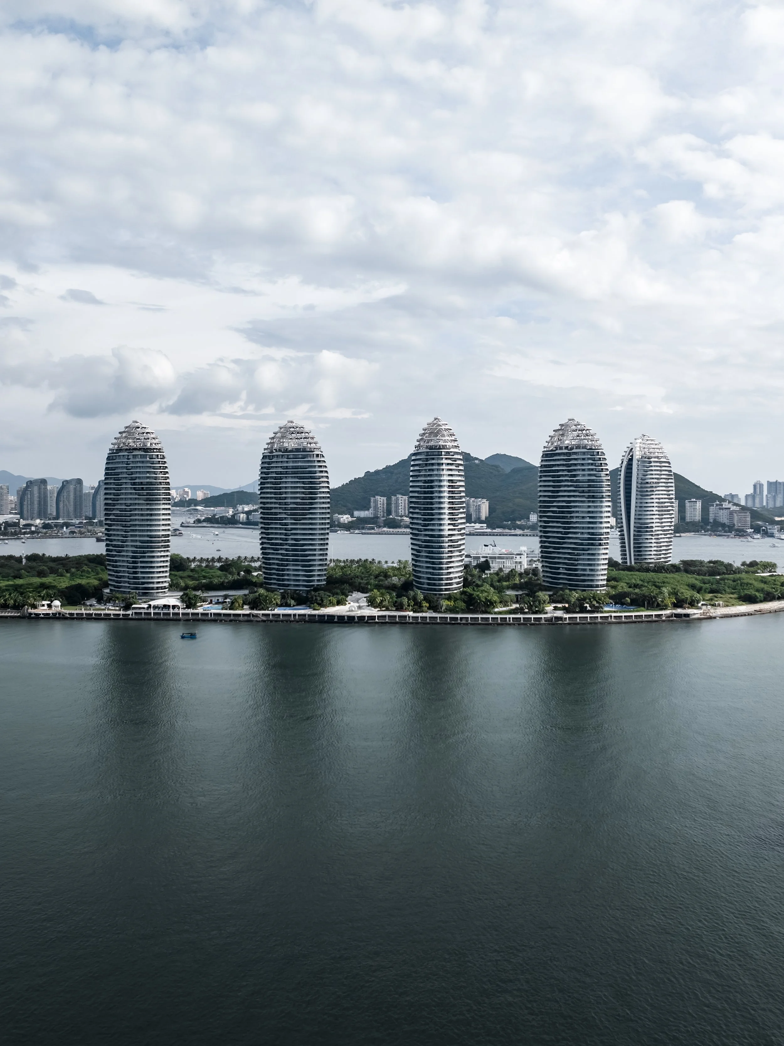 A cityscape view of modern buildings with unique architectural designs along a waterway under a cloudy sky.