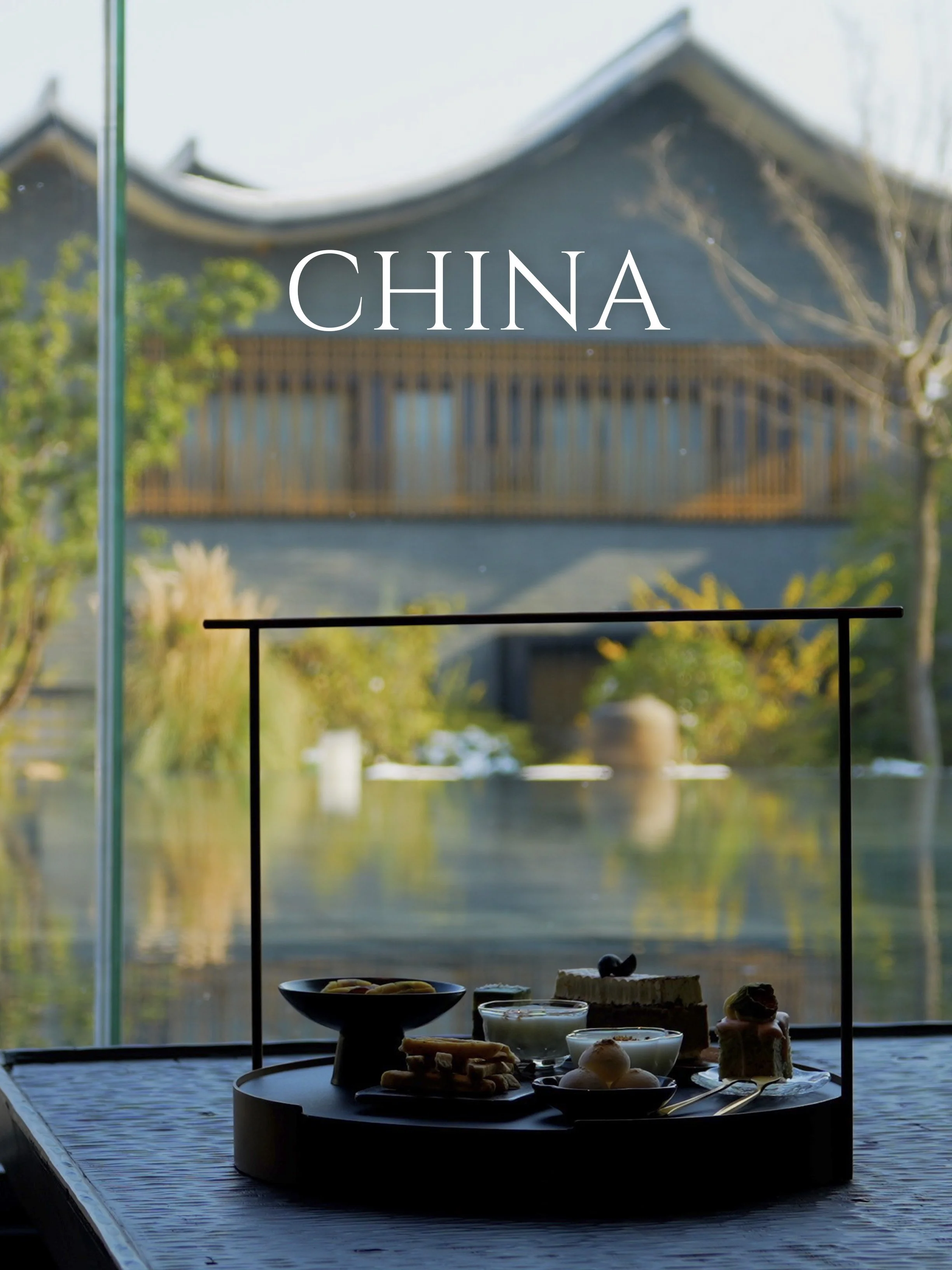 A table with various desserts and snacks near a large window showing a traditional Chinese building and trees outside.