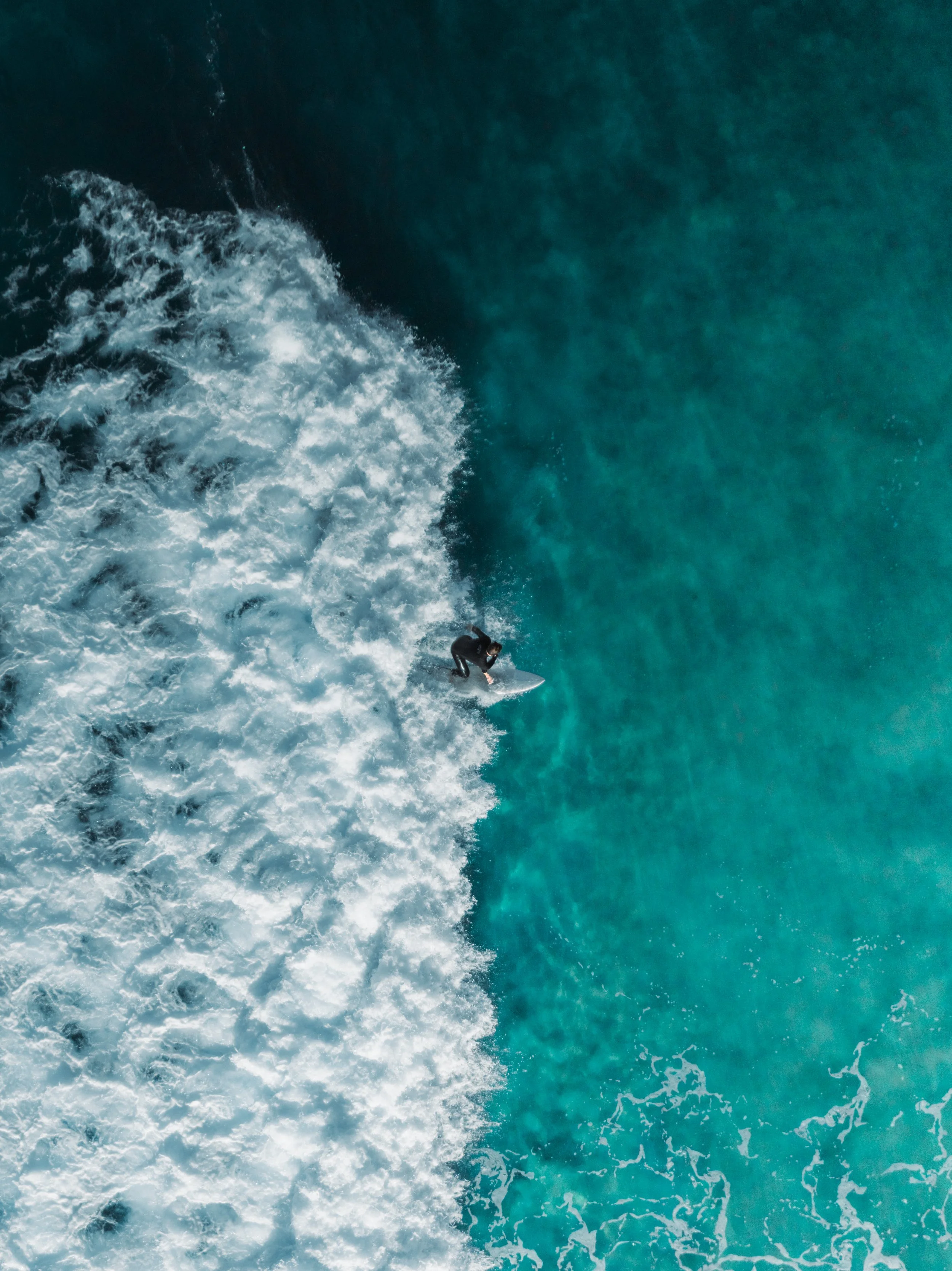 A person surfing on a wave in the ocean, with clear turquoise water.