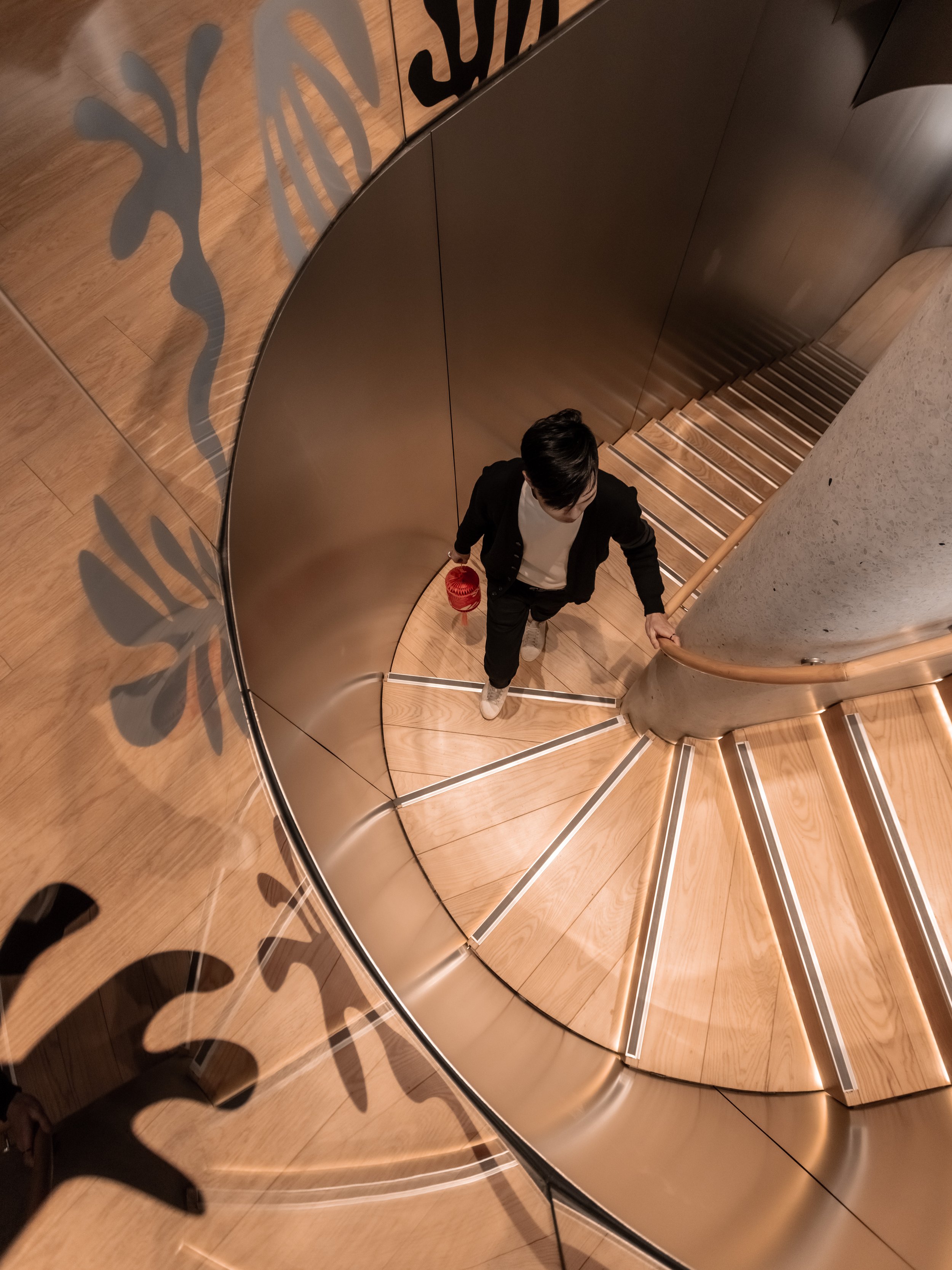 A person walking down a curved staircase holding a small red lantern.