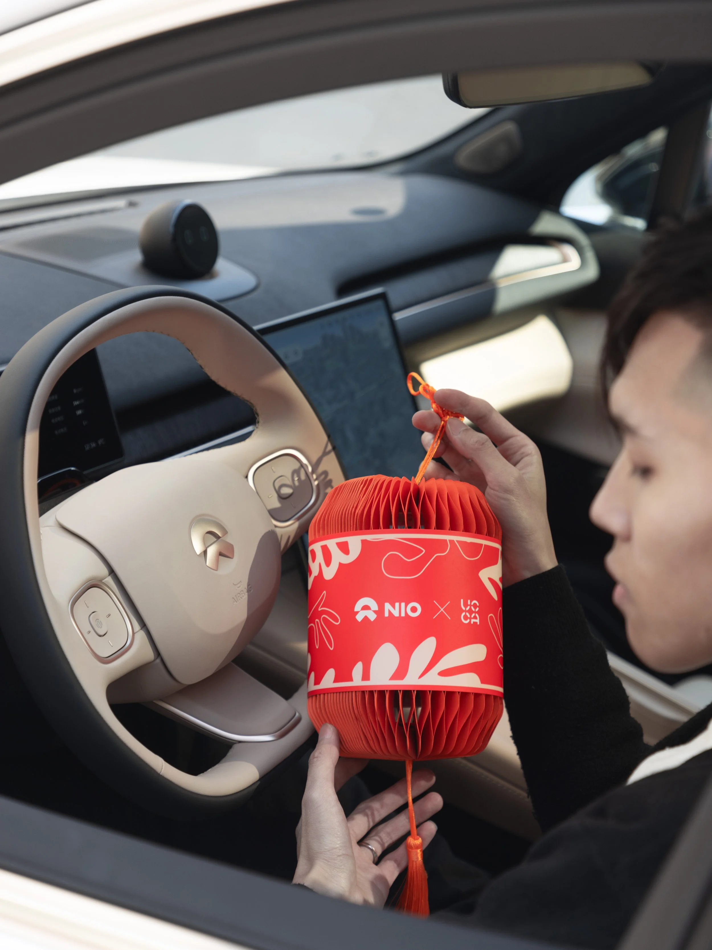 Person placing an orange paper lantern into a car, near the steering wheel, with a digital screen on the dashboard, inside a modern vehicle.