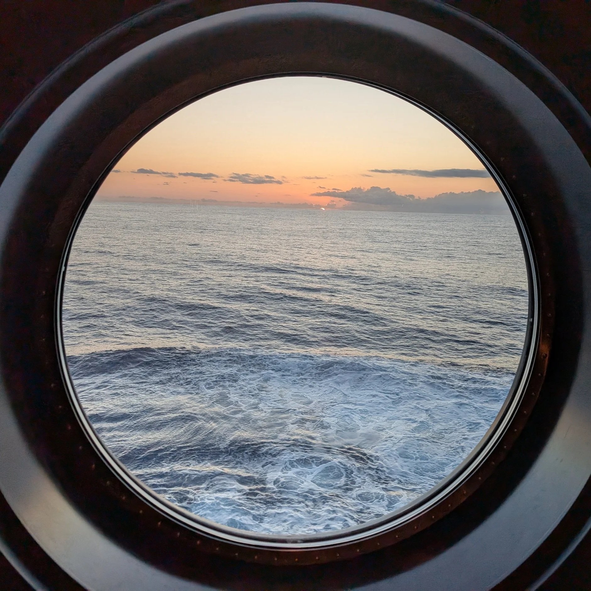 Sunset view over the ocean seen through an airplane window with a rounded frame.