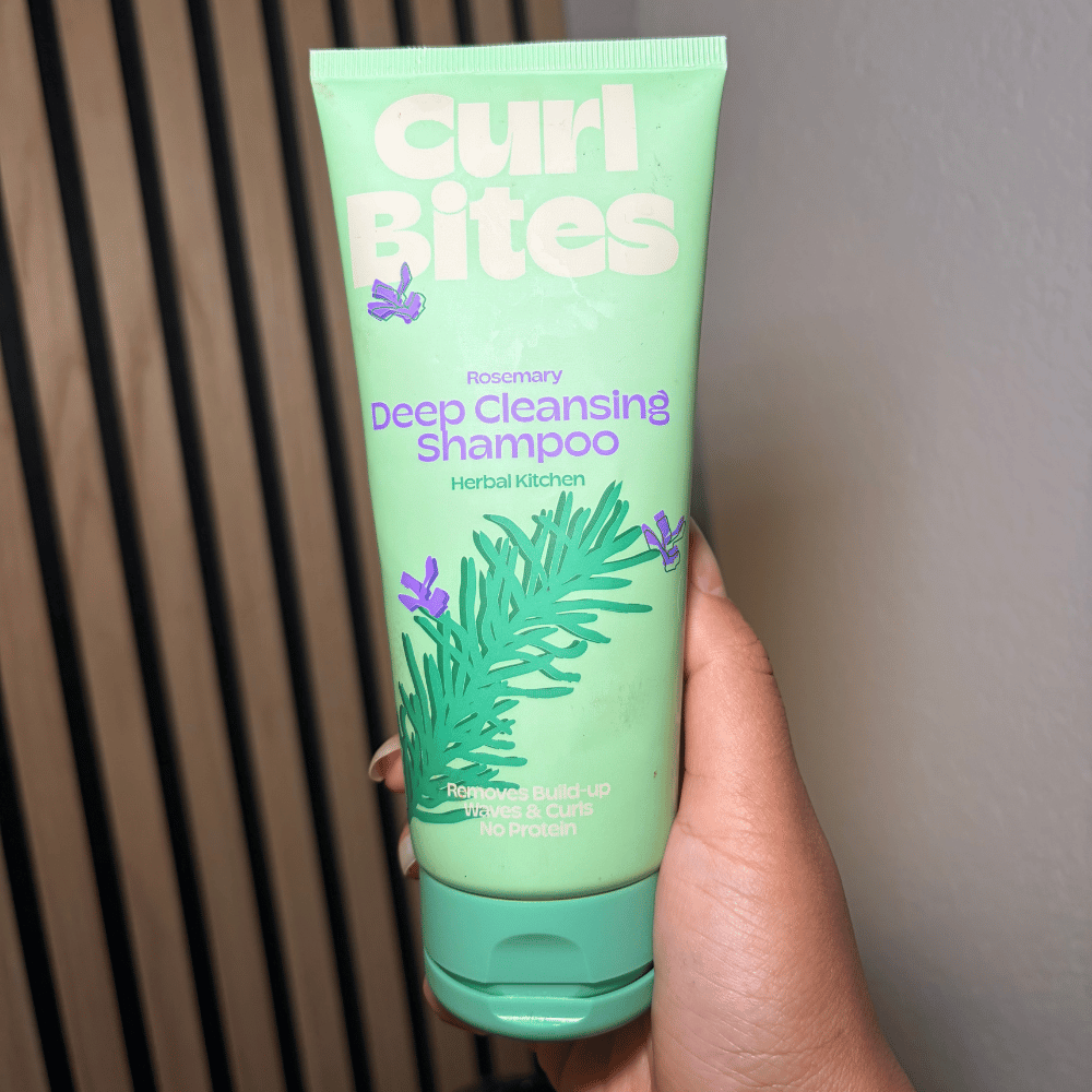 Haarstylist Lala houdt een flacon Curl Bites Rosemary Deep Cleansing shampoo vast