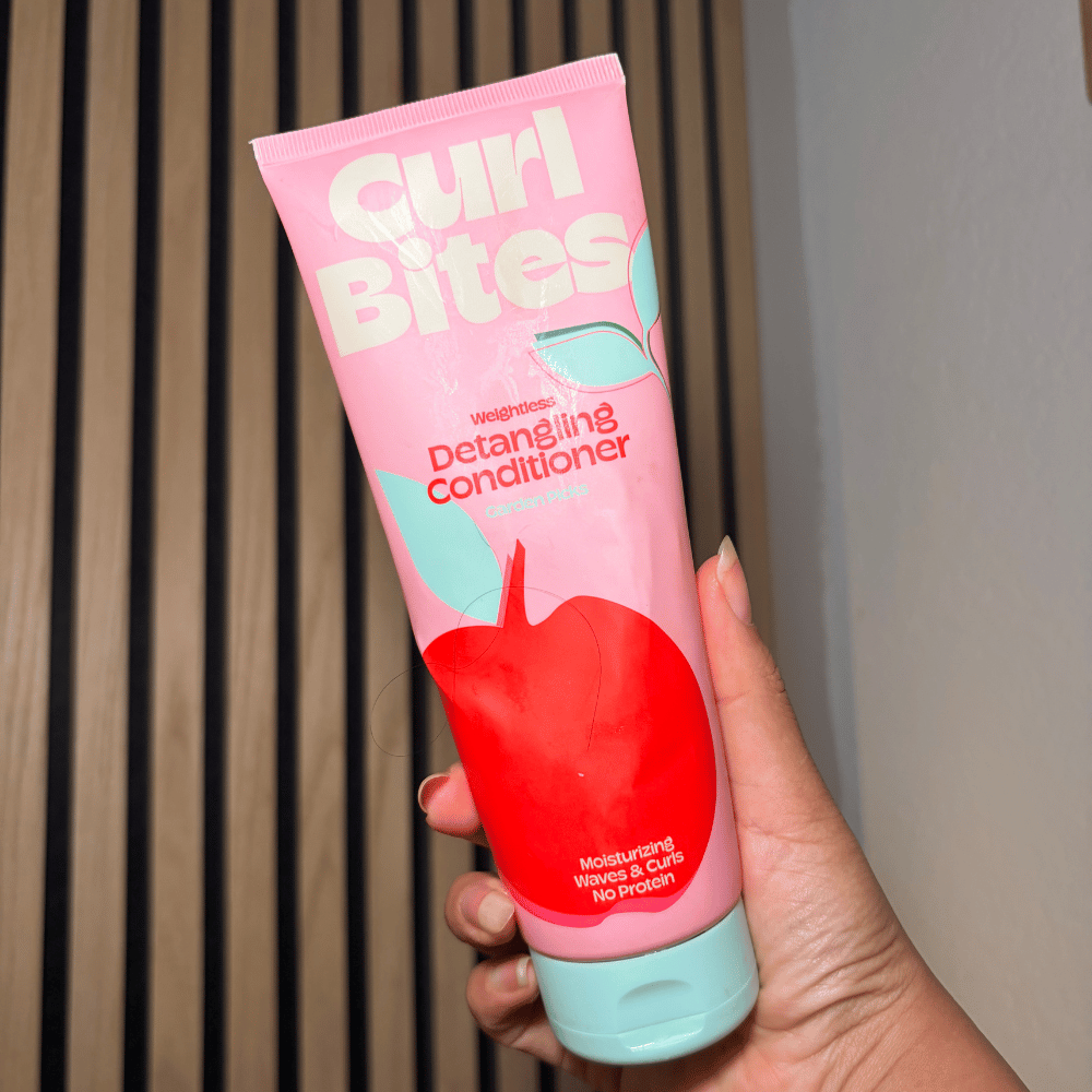 Haarstylist Lala toont een roze flacon Curl Bites Weightless Detangling Conditioner