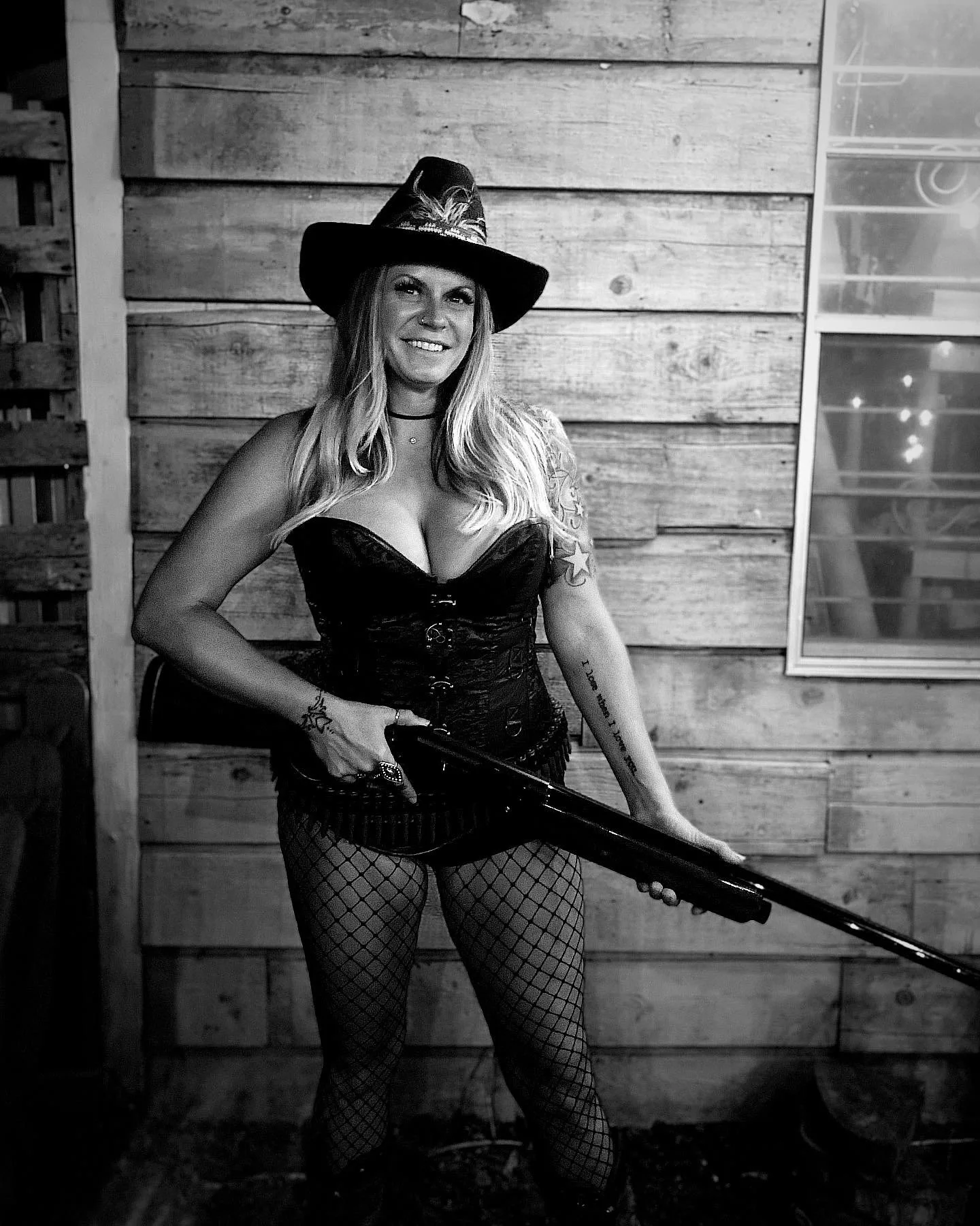 A woman dressed in a witch costume holding a broomstick, standing in front of a wooden wall.